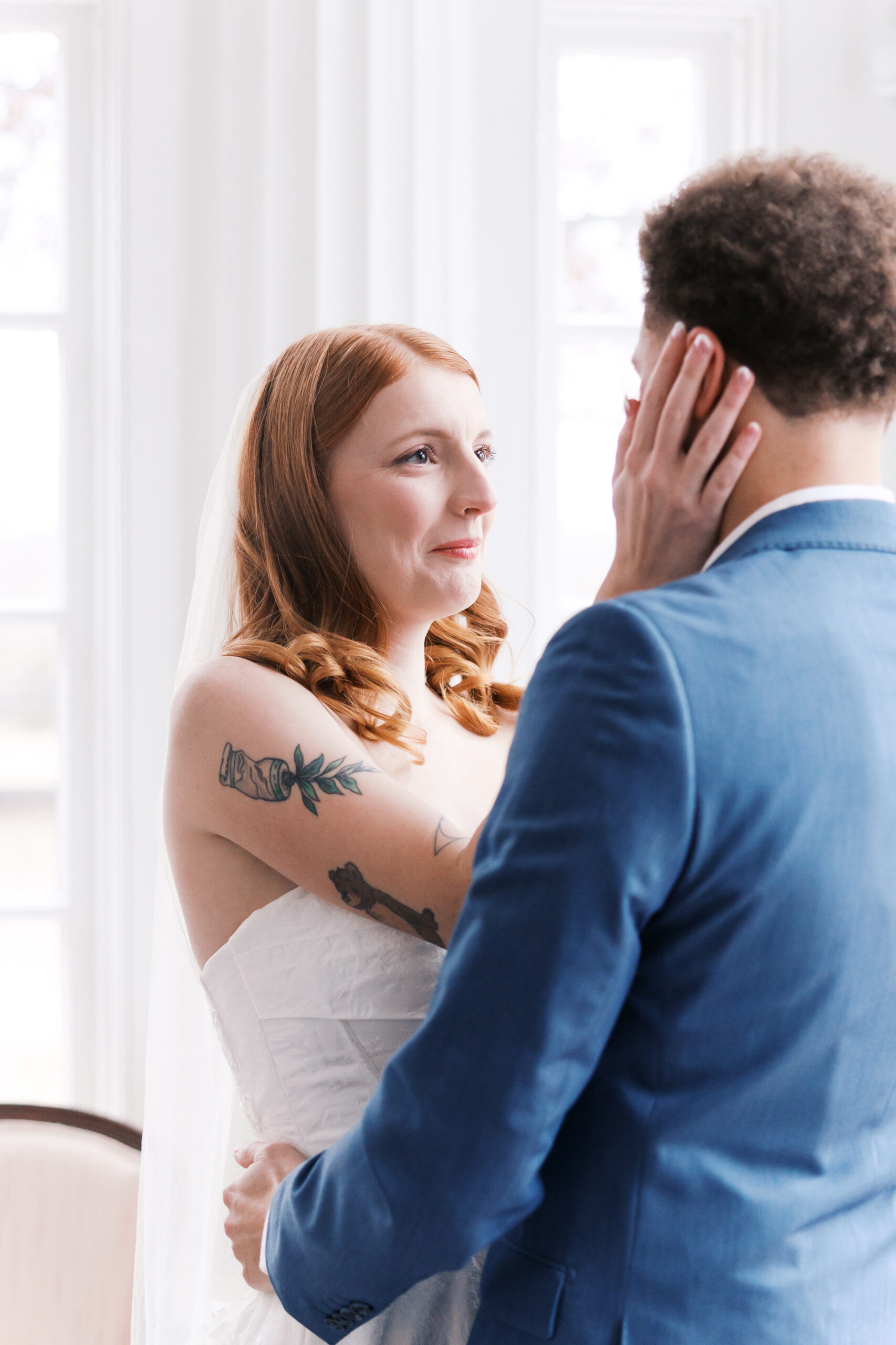 Bride touching groom’s face during intimate vow exchange by window