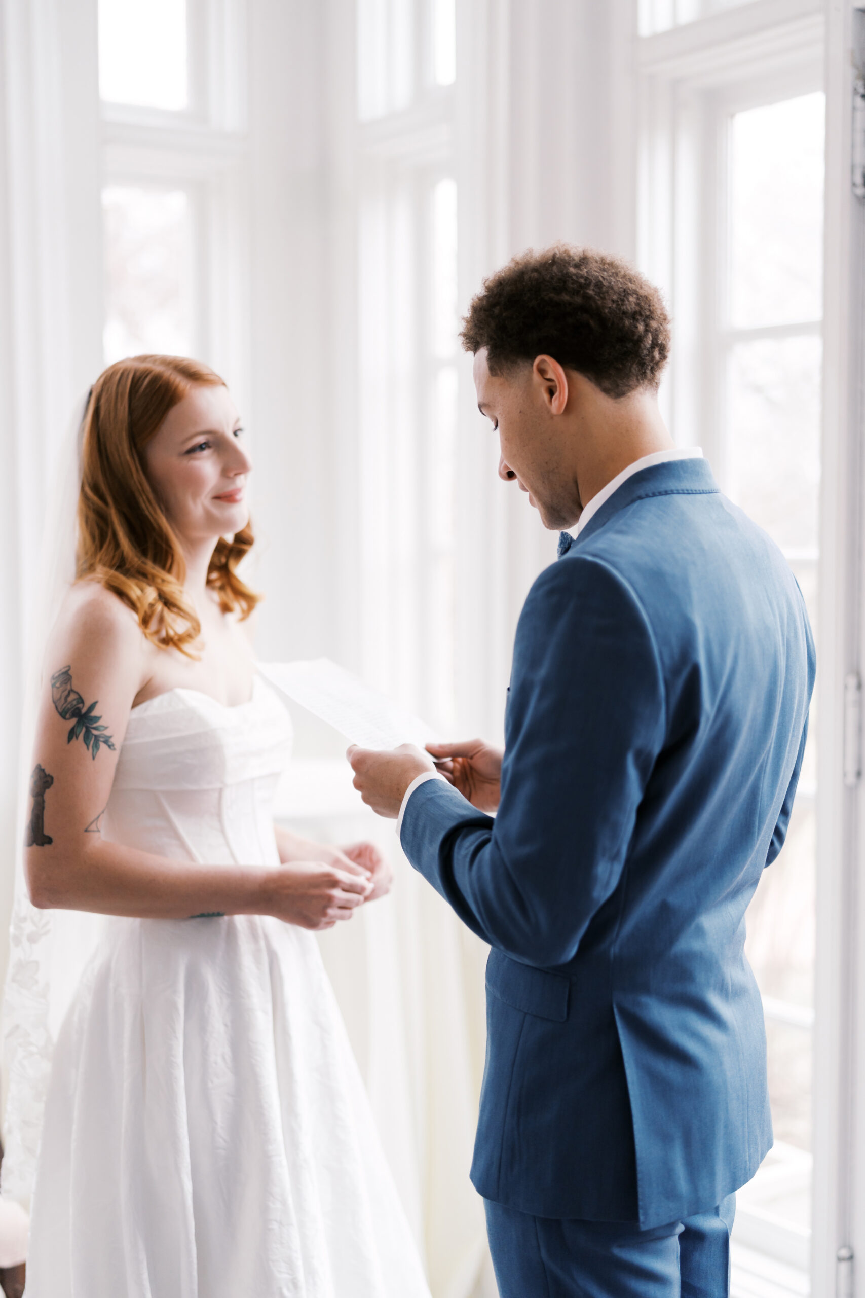 Bride and groom exchanging vows indoors by tall windows in soft natural light
