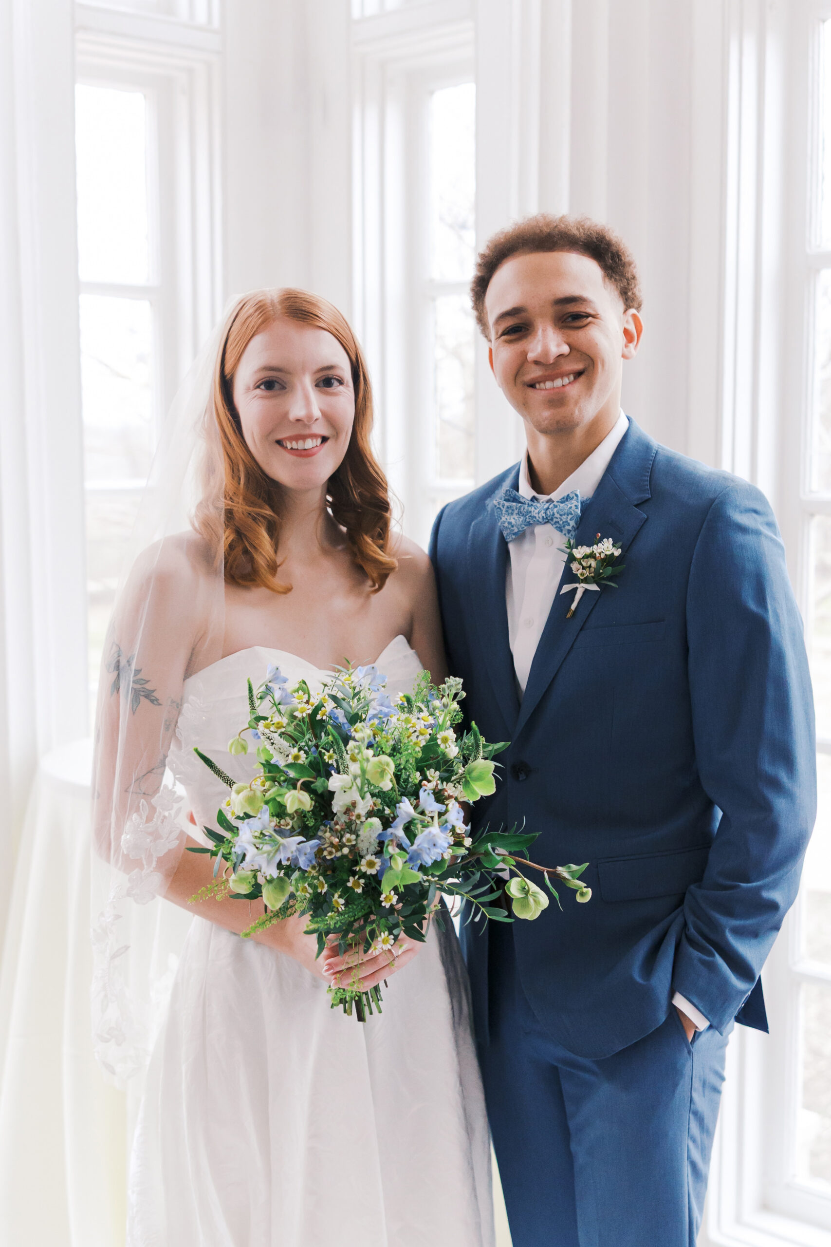 Bride and groom smiling while holding bouquet in bright indoor wedding portrait