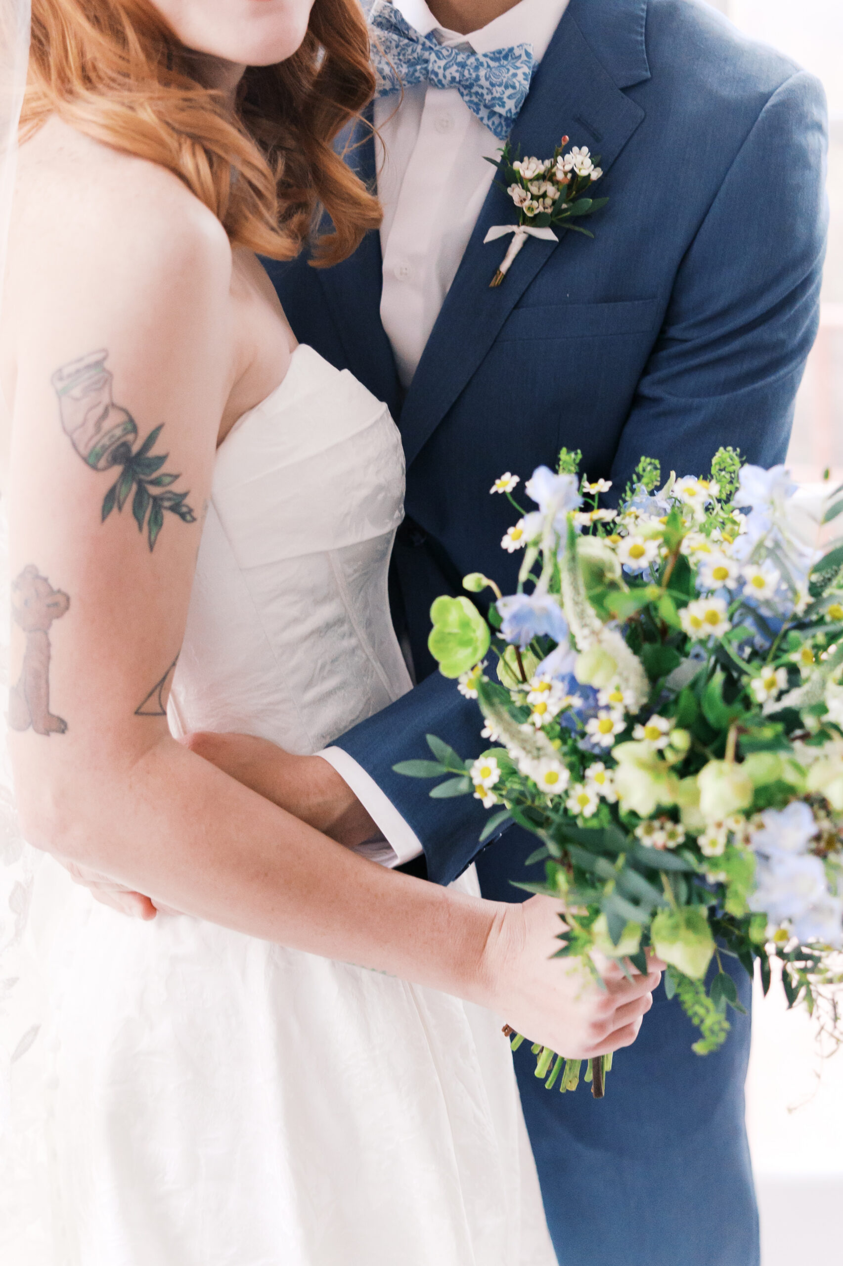 Close-up of bride and groom embracing with blue suit and white dress details
