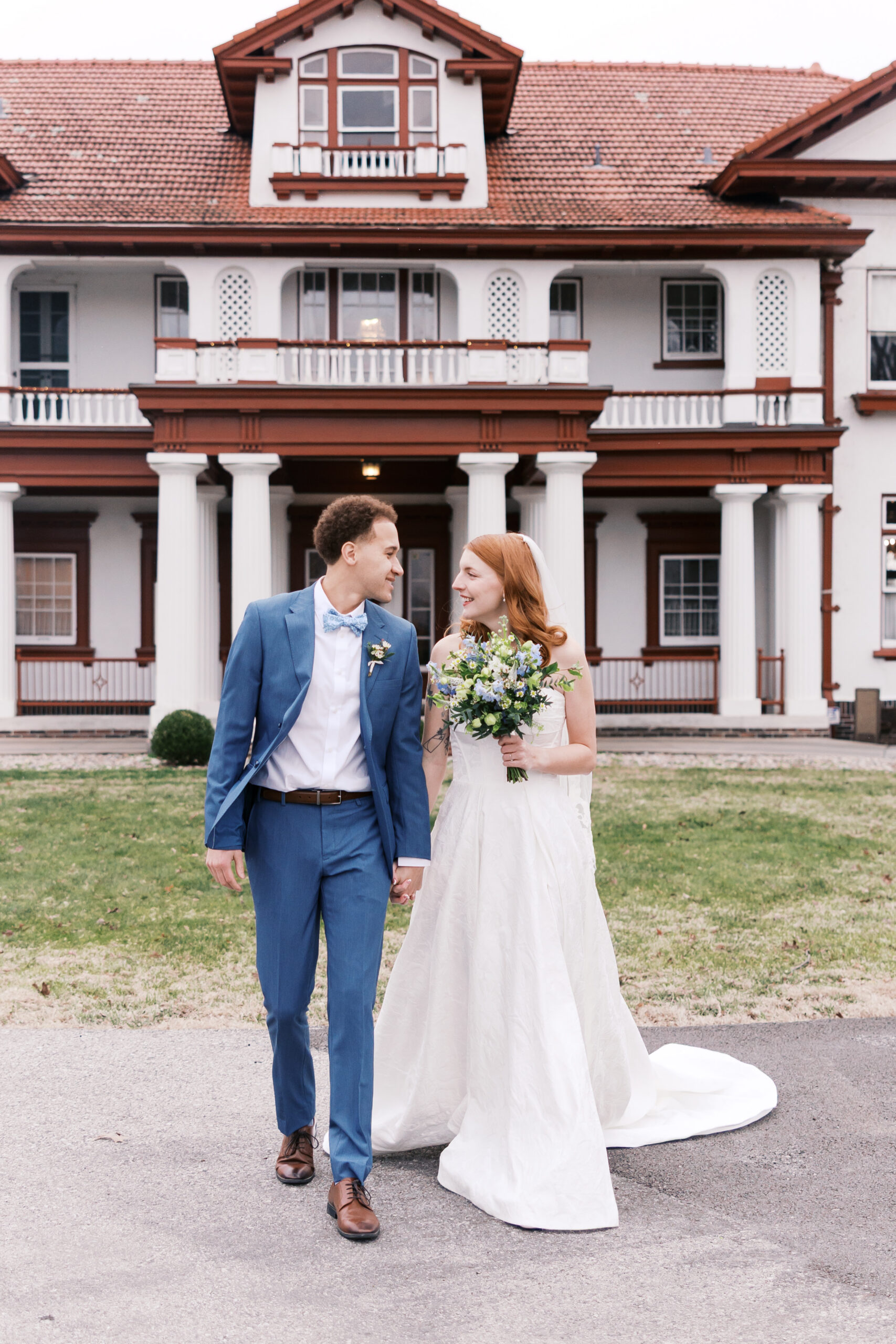 Bride and groom walking hand in hand in front of large historic wedding venue