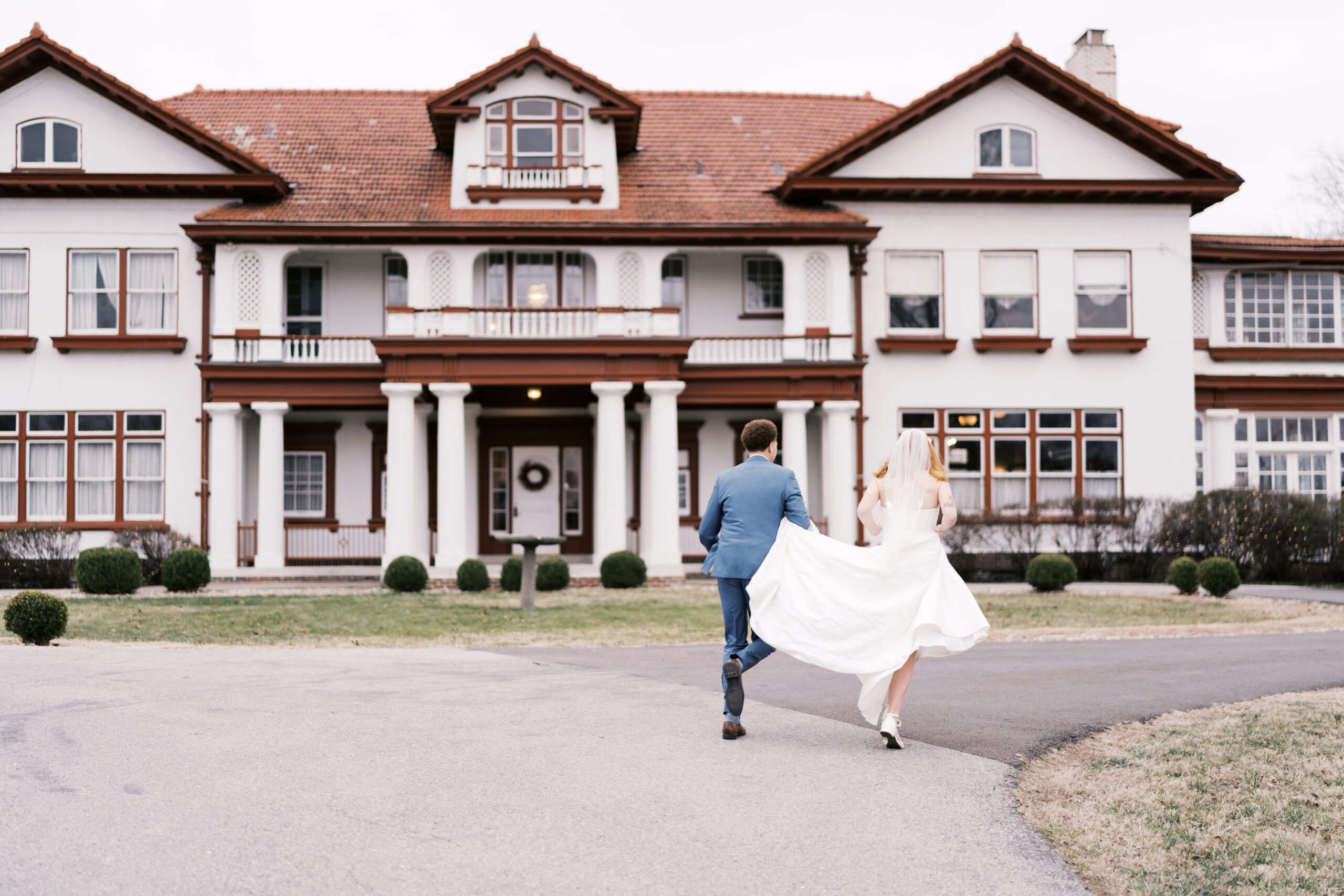 Bride and groom running toward large estate venue with flowing wedding dress