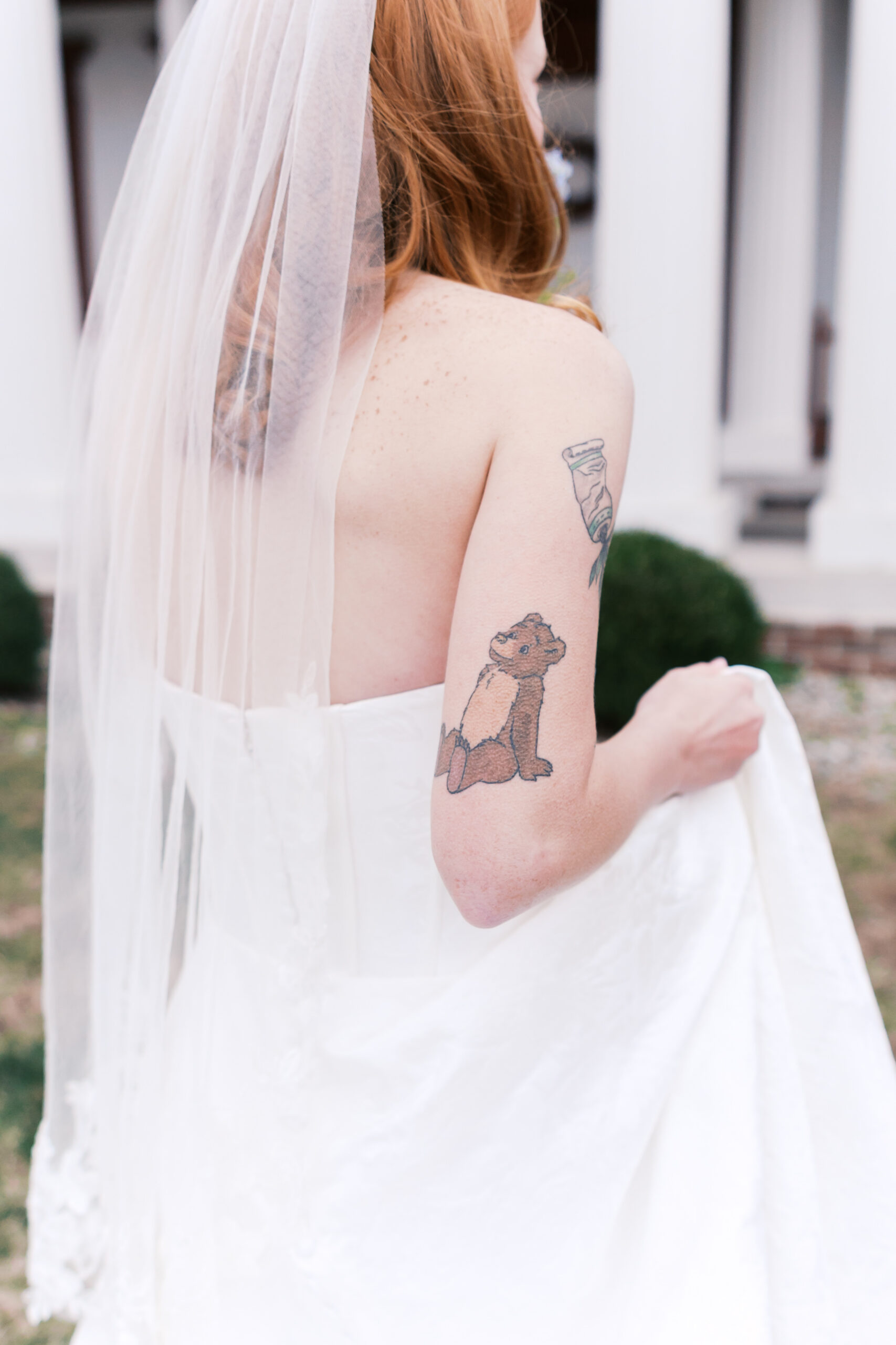 Close-up of bride’s veil and arm tattoos while holding dress outdoors