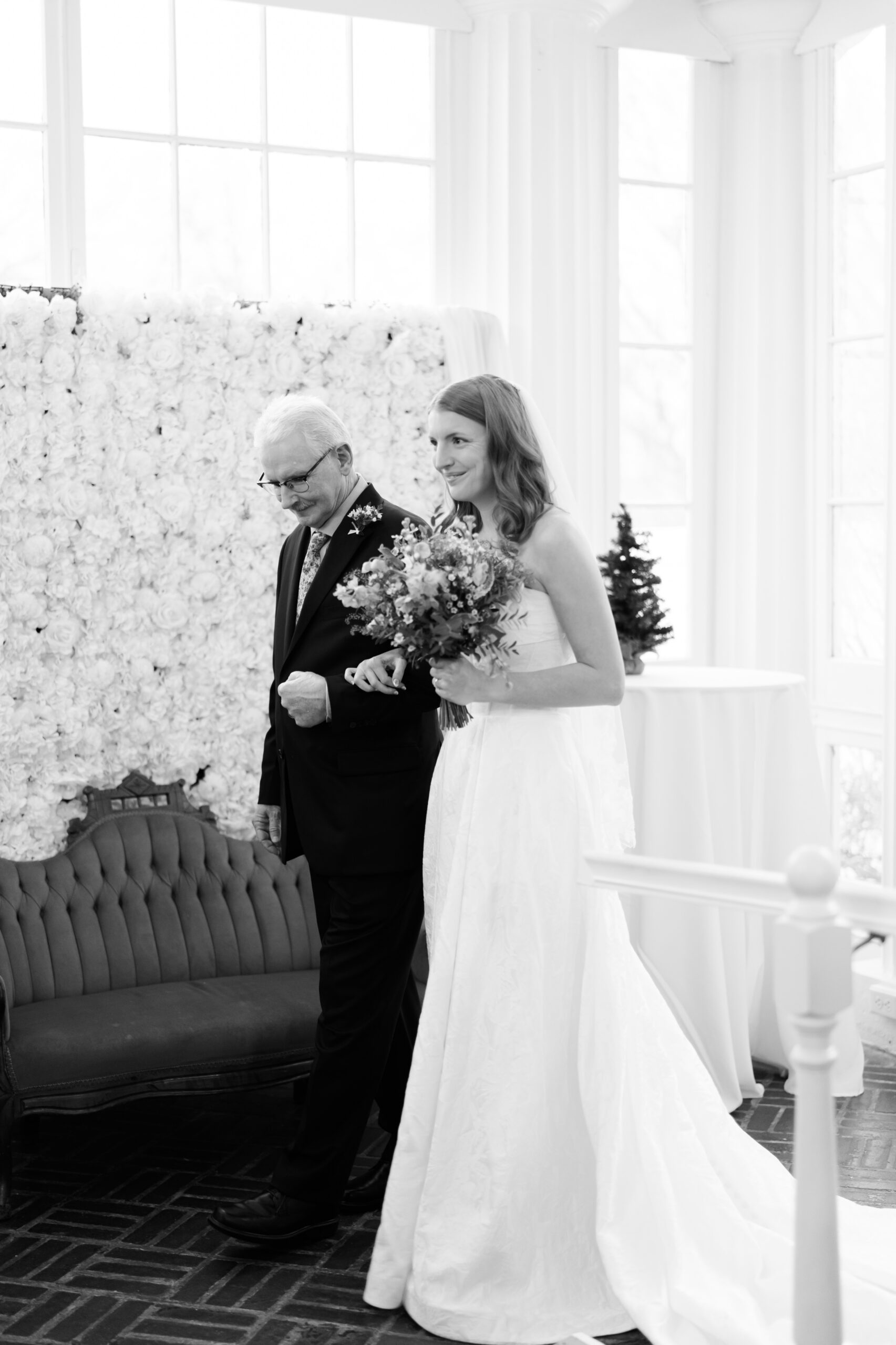Bride walking with older man down aisle holding bouquet indoors