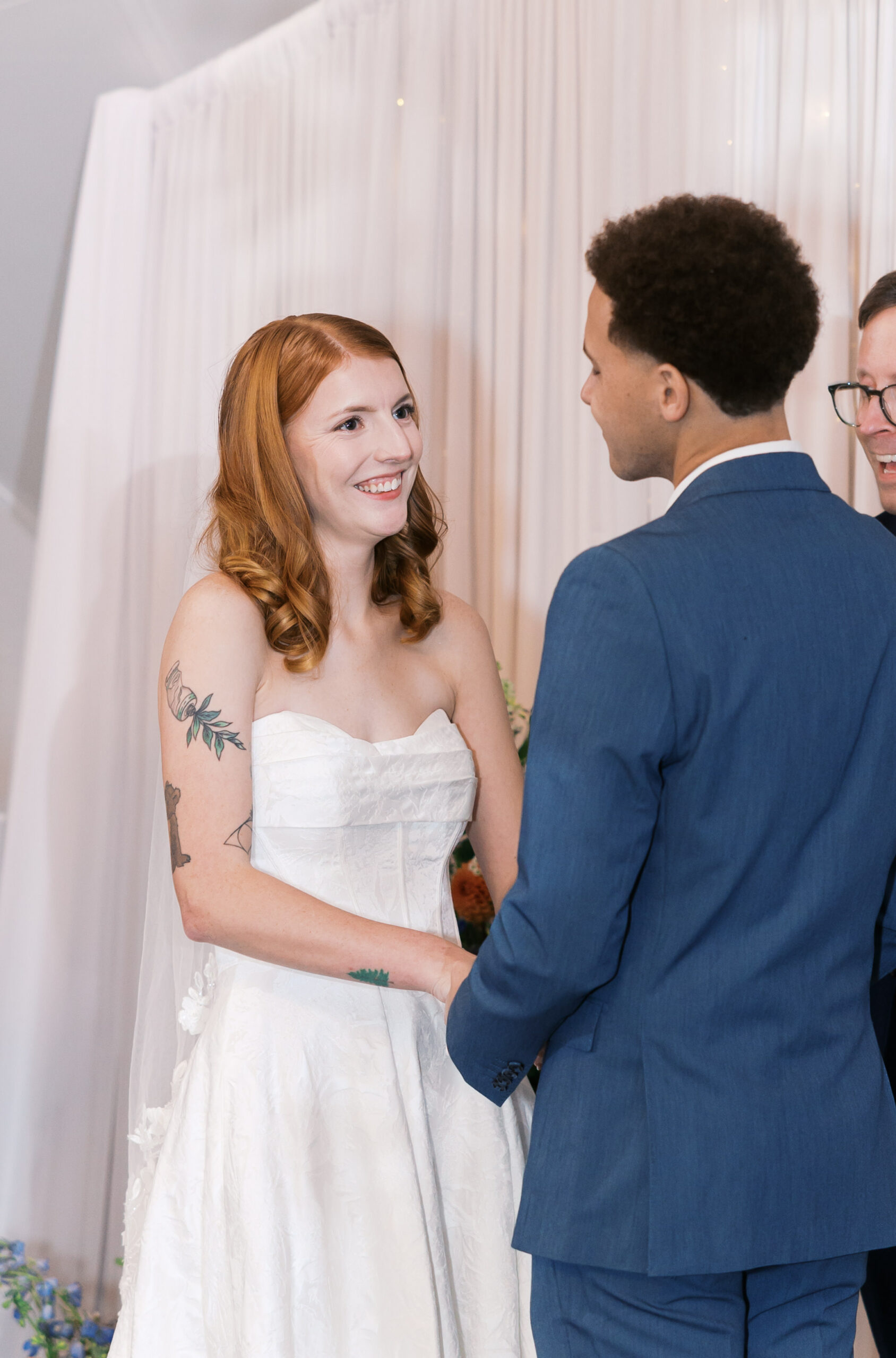 Close-up of bride and groom holding hands and smiling during wedding vows.
