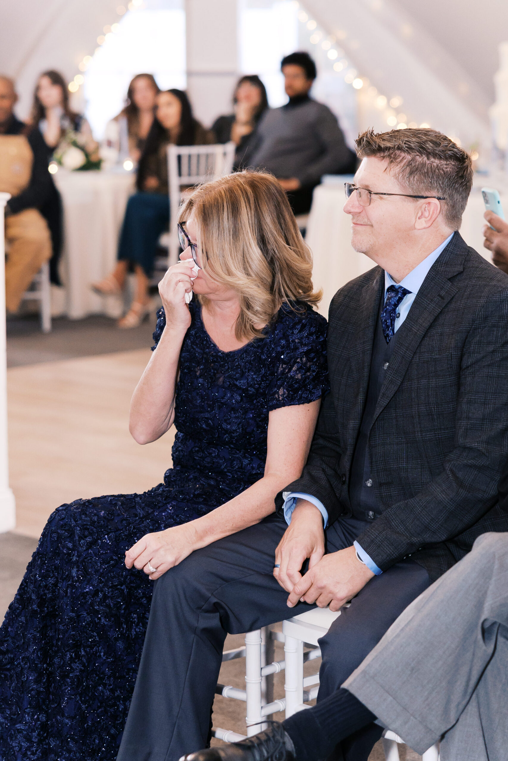 Guests seated during ceremony, woman wiping eye while watching emotional wedding moment.
