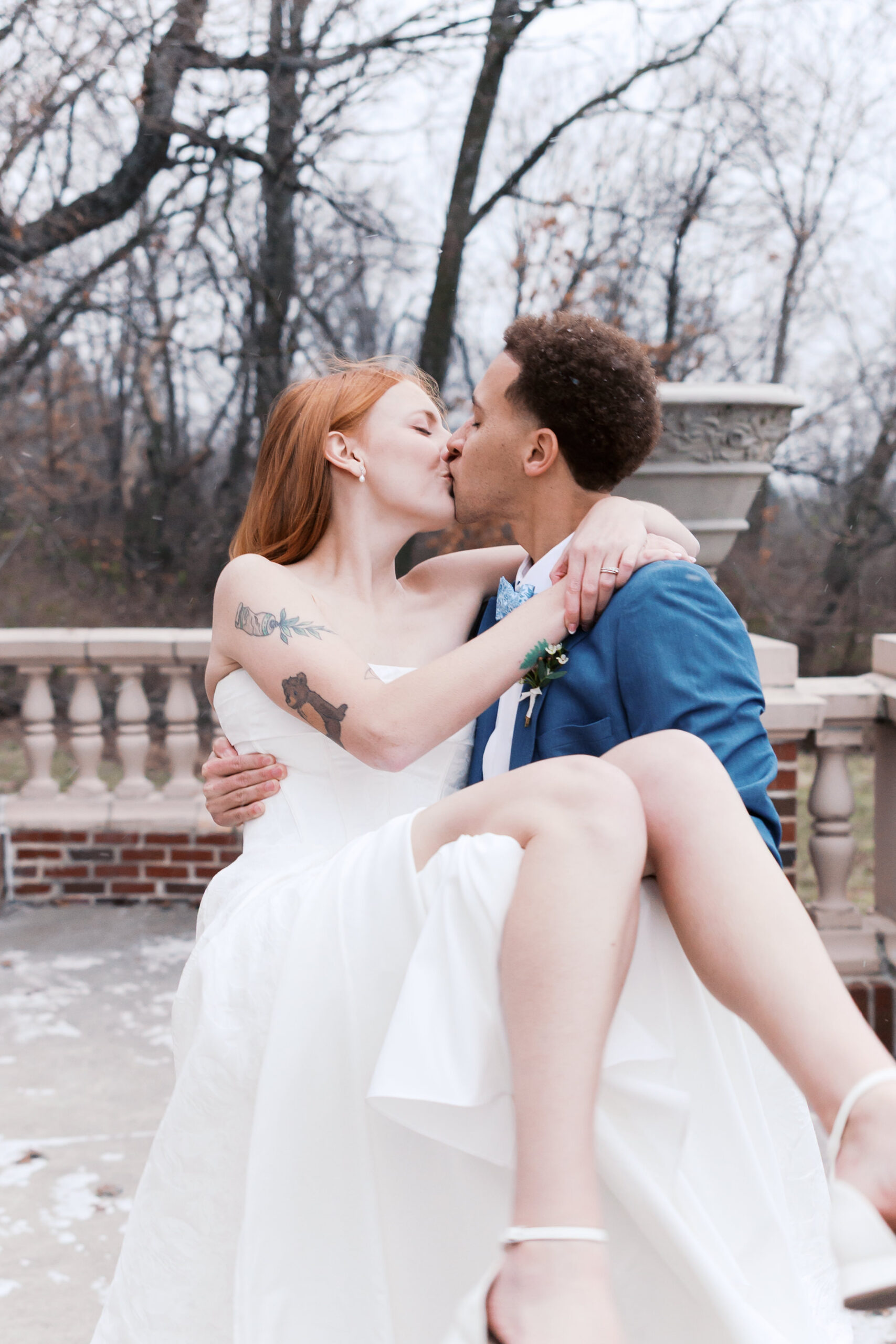 Bride and groom kiss as groom carries bride on stone patio.