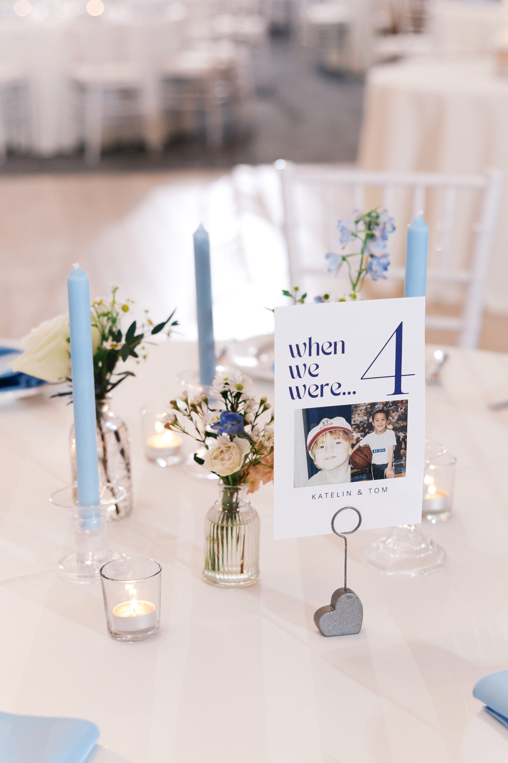 Wedding table centerpiece with blue candles, small floral arrangements, and “when we were” photo table number sign