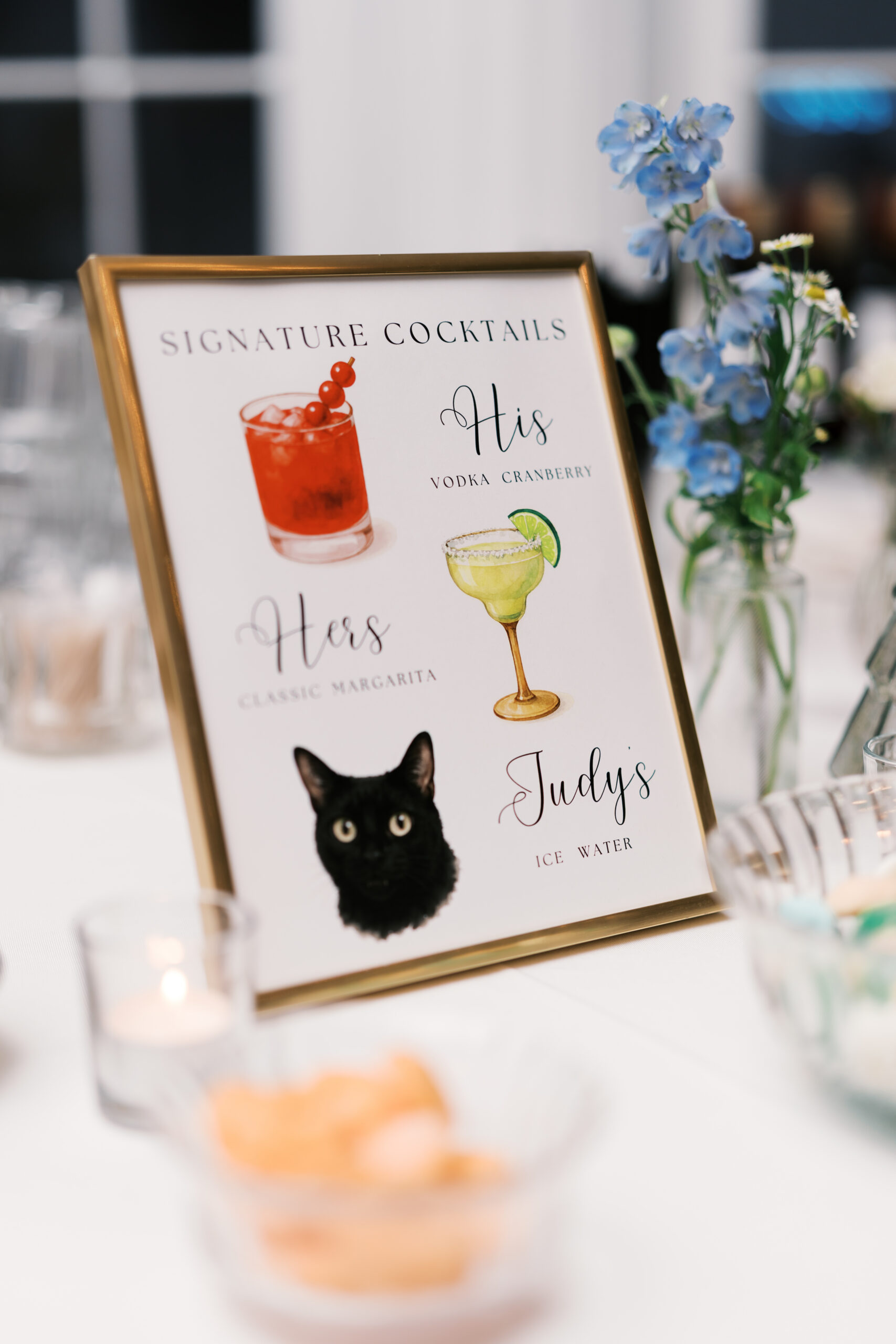 Framed wedding signature cocktail sign with illustrated drinks and black cat graphic on decorated table
