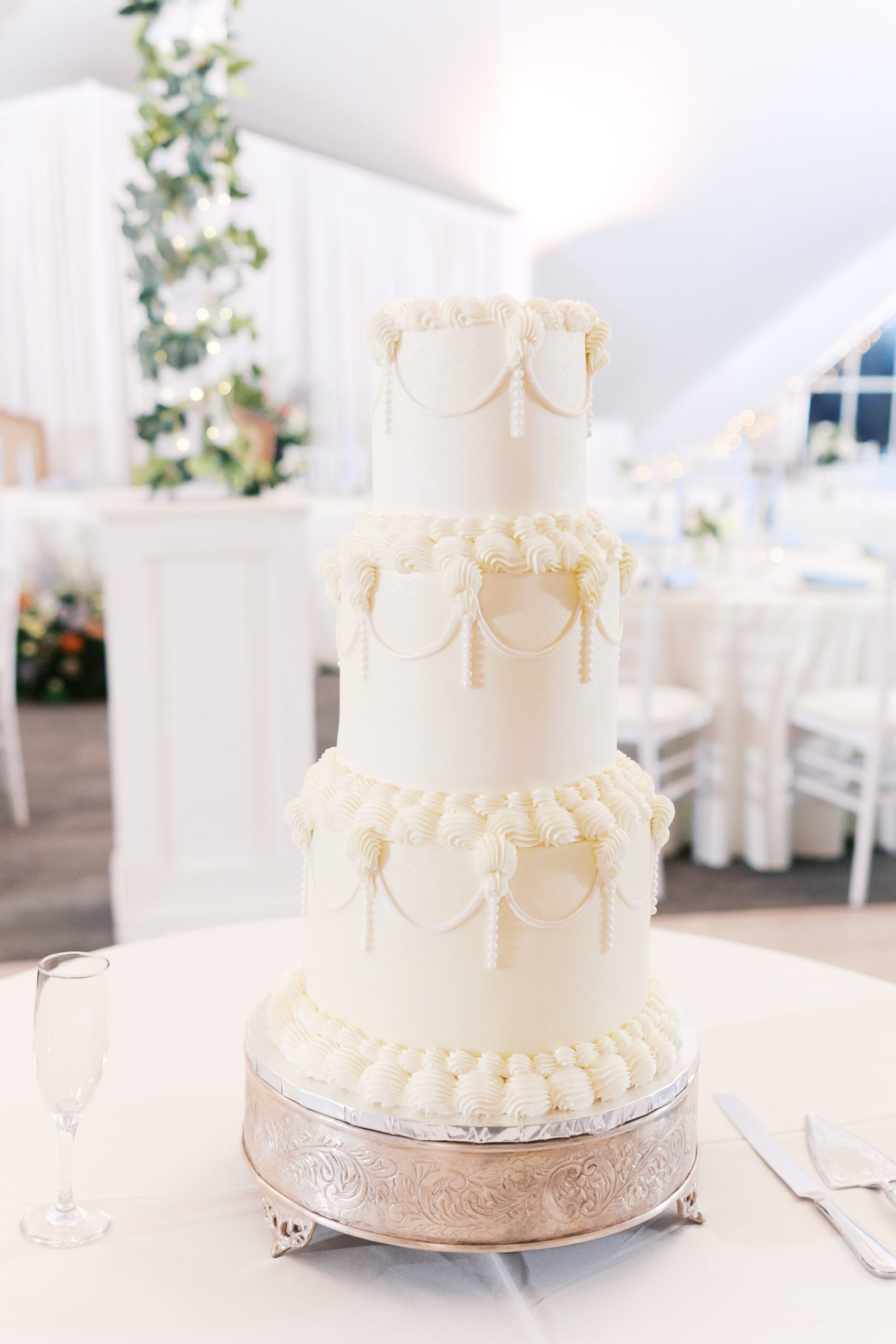 Three-tier white wedding cake with piped frosting details on silver stand in reception space