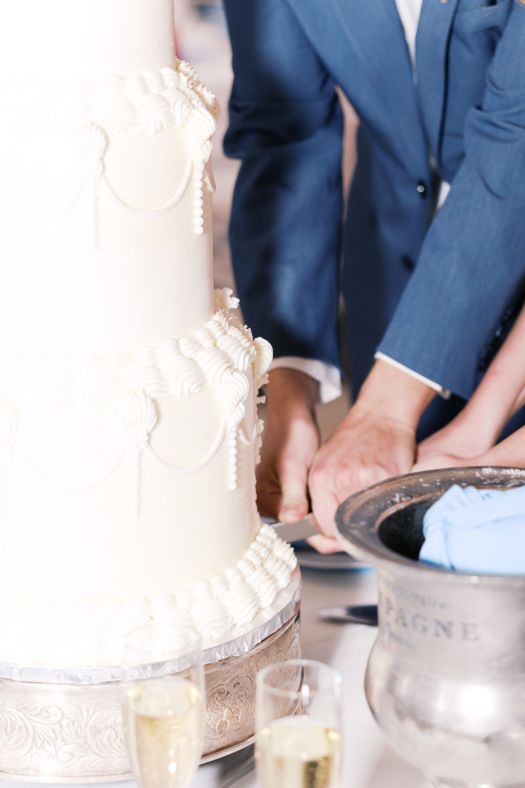 Close up of couple cutting a tiered wedding cake beside champagne bucket and glasses