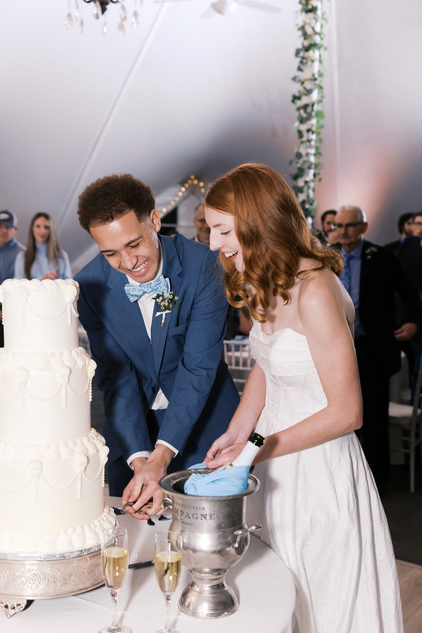 Couple cutting a tiered wedding cake beside champagne bucket and glasses