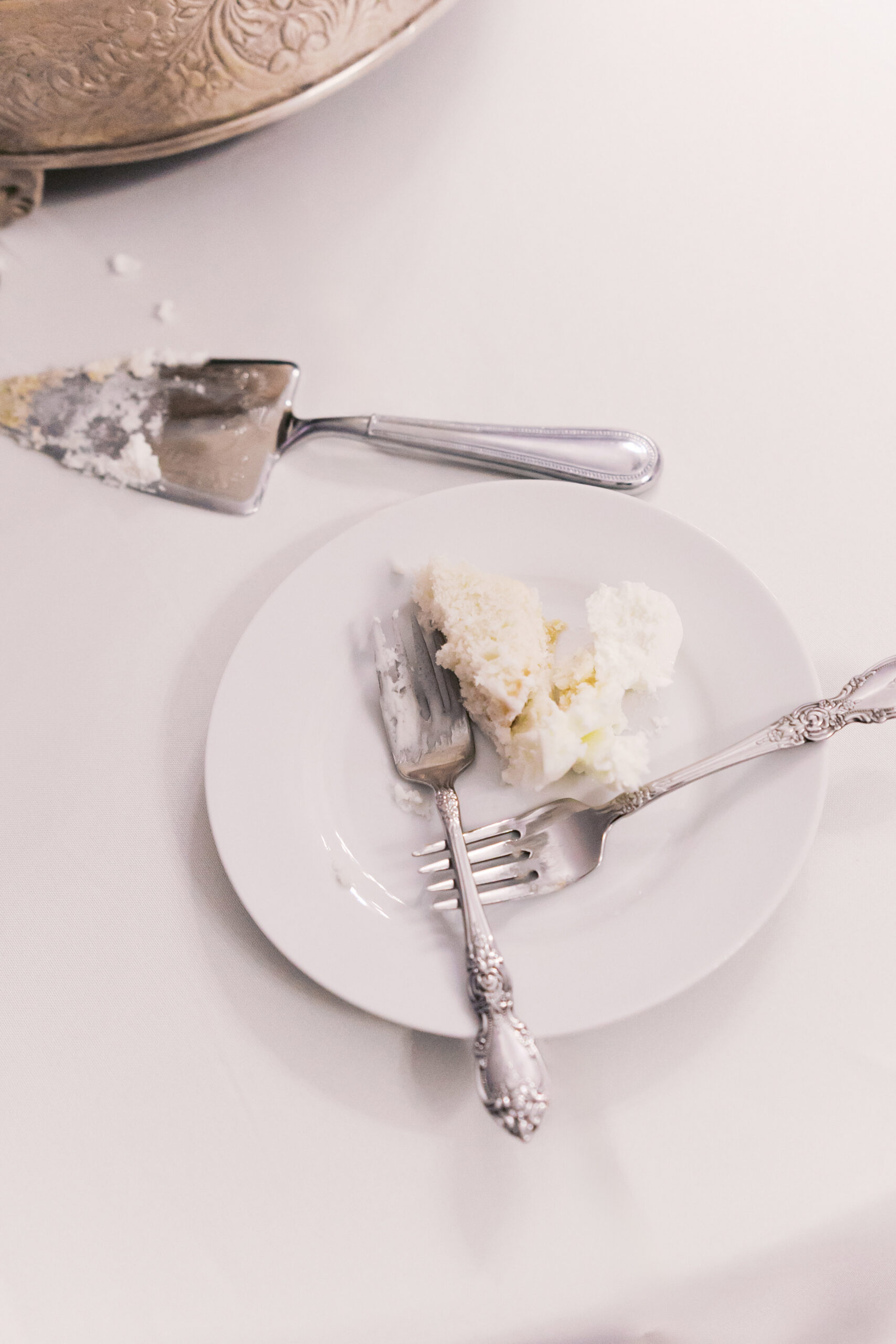 Slice of white wedding cake on plate with forks and cake server on table