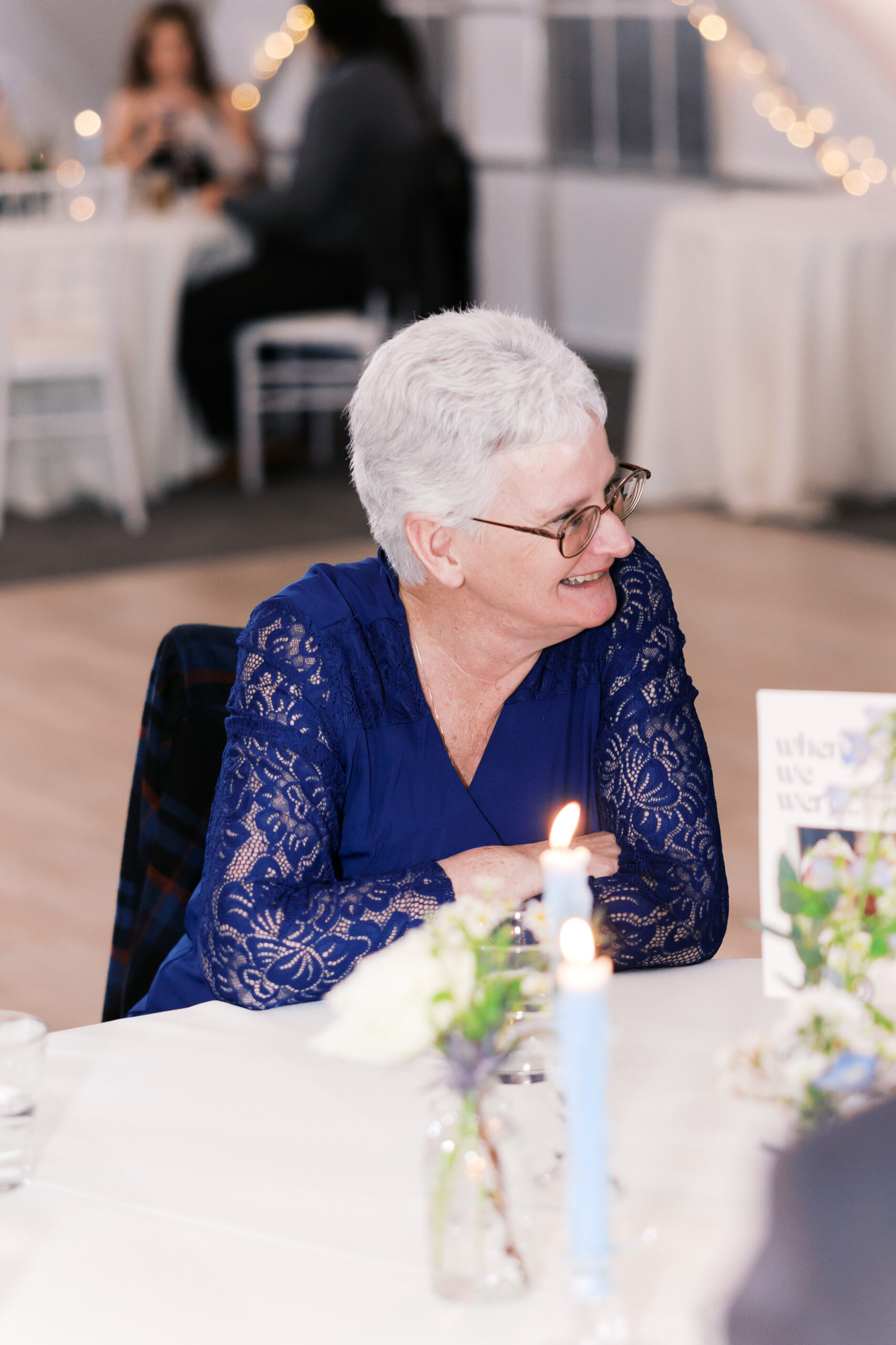Guest in navy lace dress seated at reception table with candles and floral centerpiece