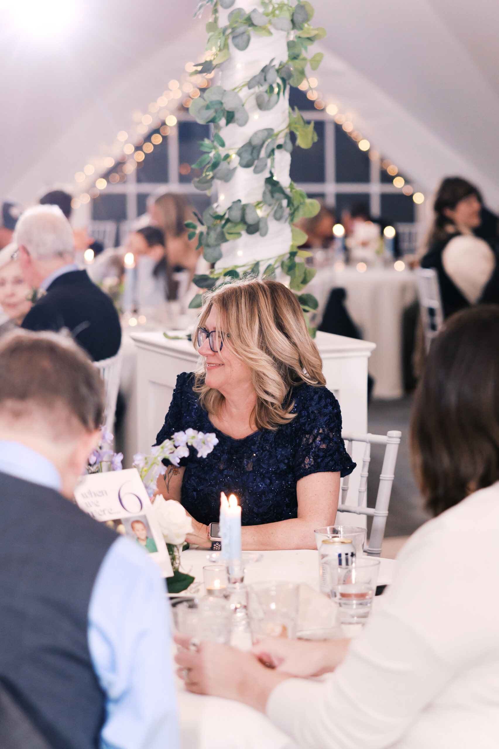 Wedding guests seated at round tables under string lights inside reception tent