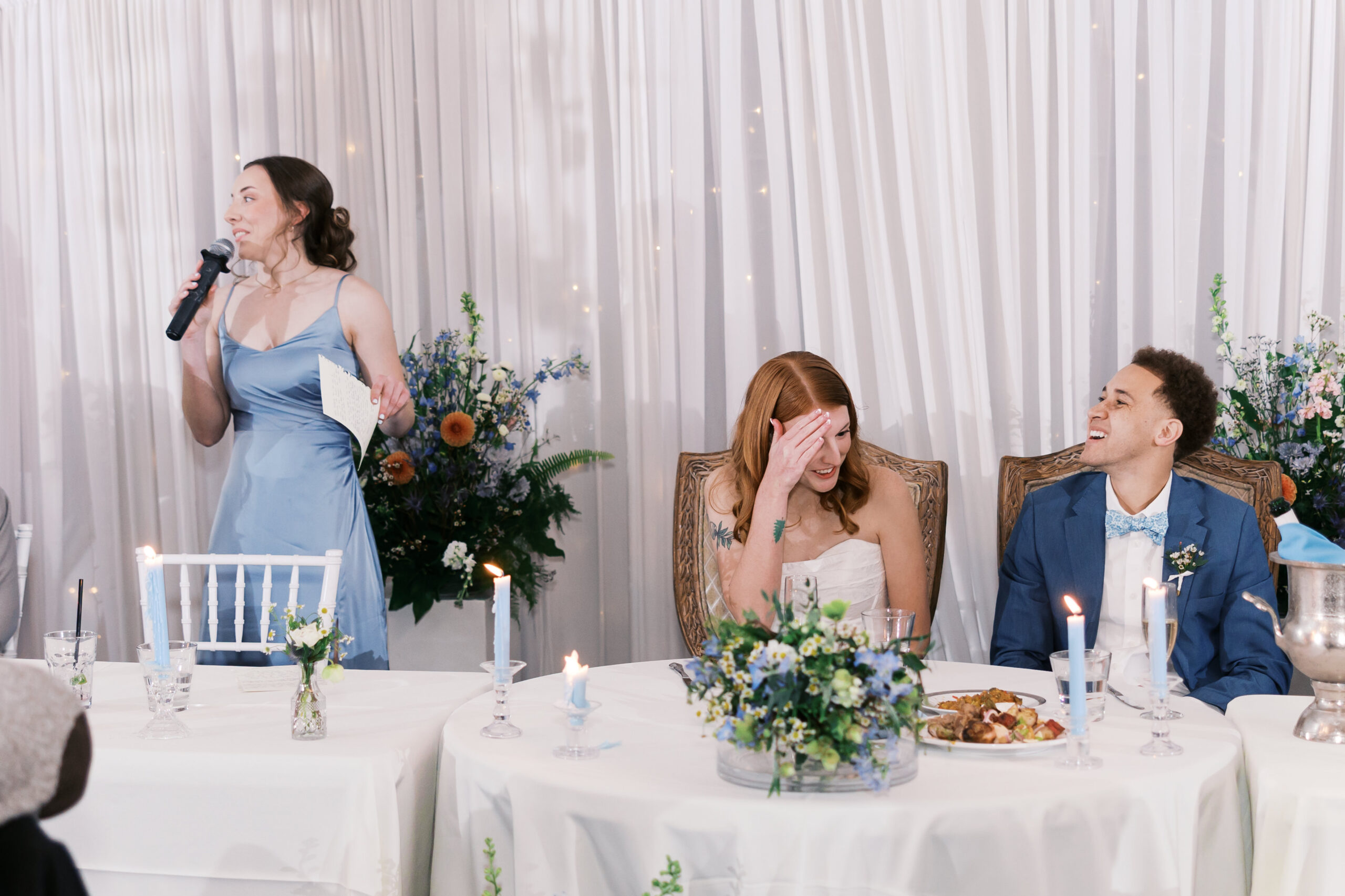 Bride and groom reacting during speech at decorated sweetheart table with candles and florals