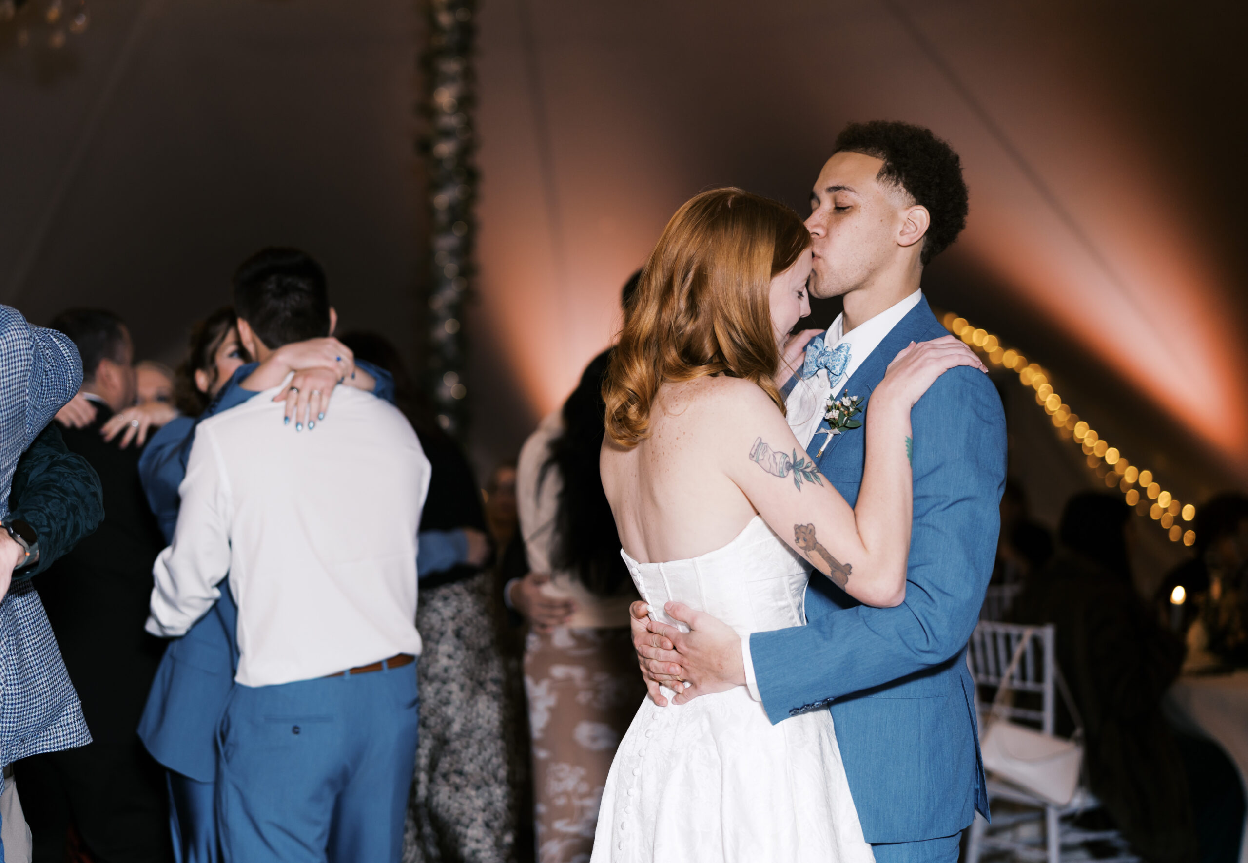 Bride and groom share slow dance embrace under warm lighting at wedding reception.