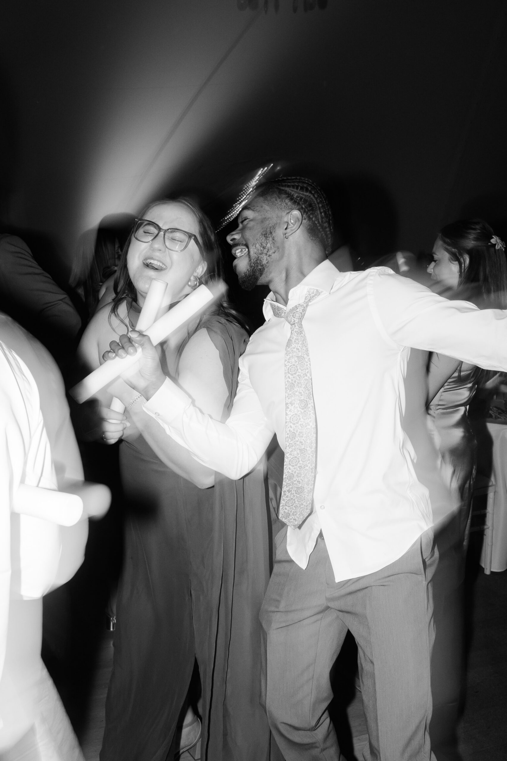 Two guests dancing closely and singing along while holding glow sticks during lively wedding reception