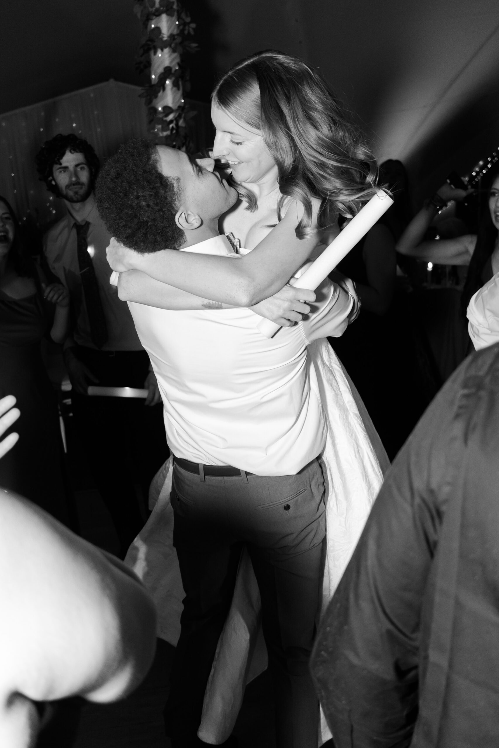 Groom lifting bride while dancing closely on crowded reception dance floor in black and white photo