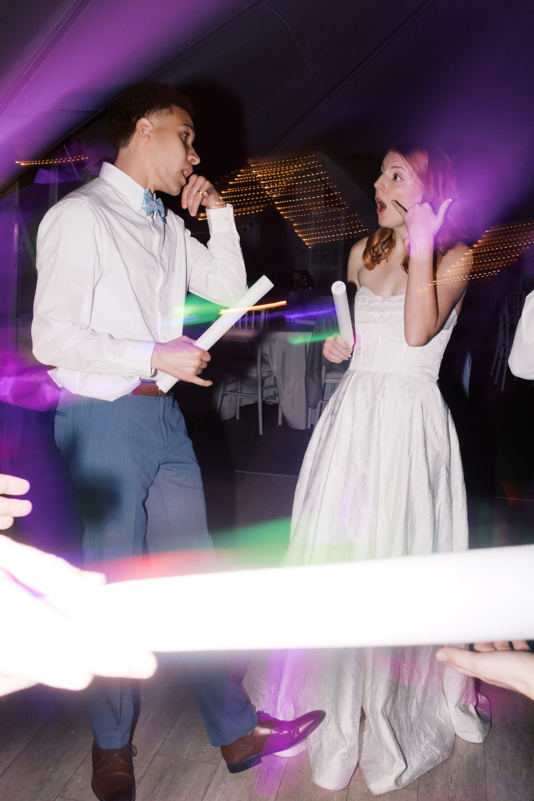 Bride and groom dancing with glow sticks under colorful lighting effects at wedding reception