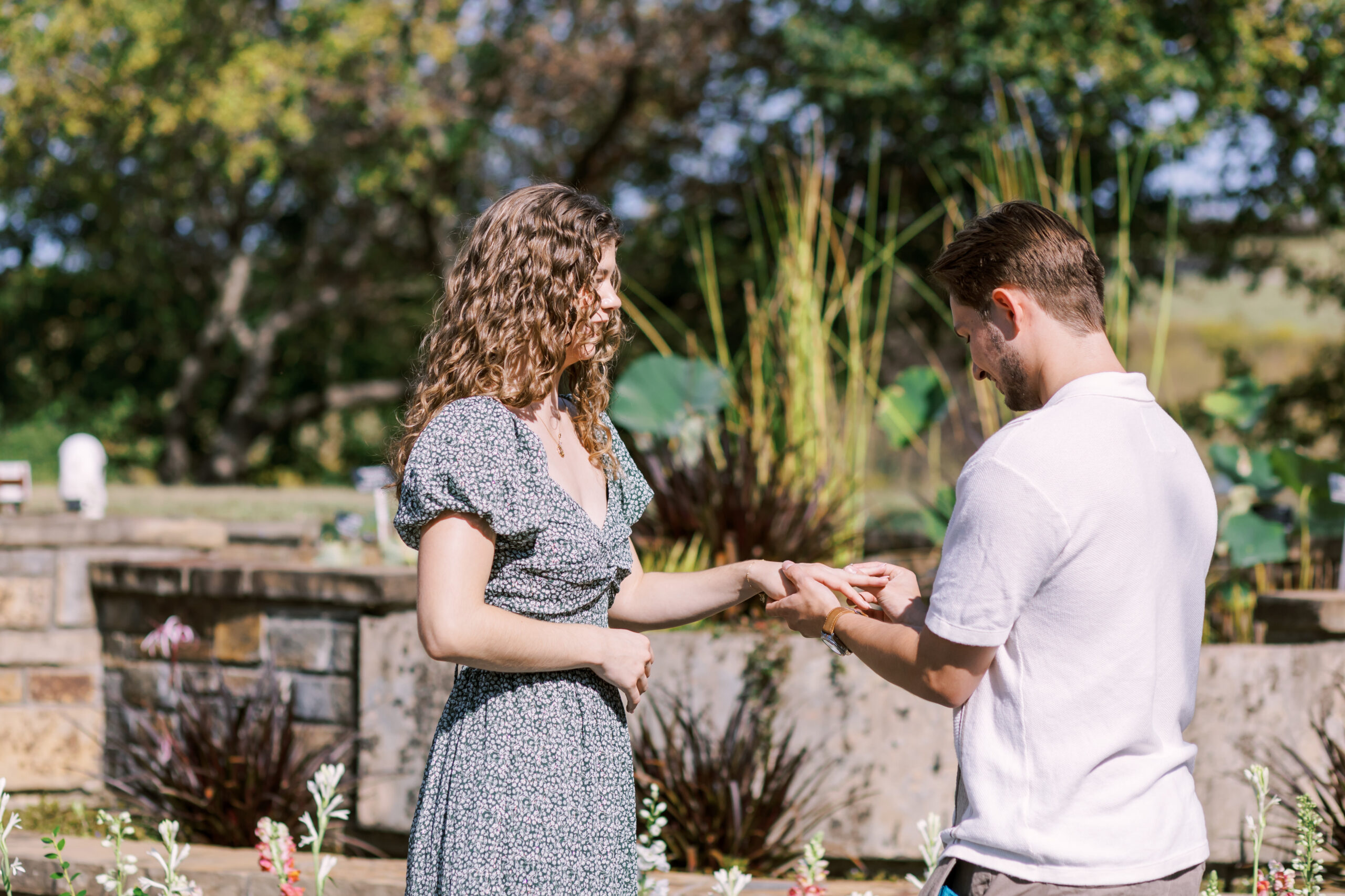Man places engagement ring on woman’s finger during outdoor proposal at Powell Gardens.
