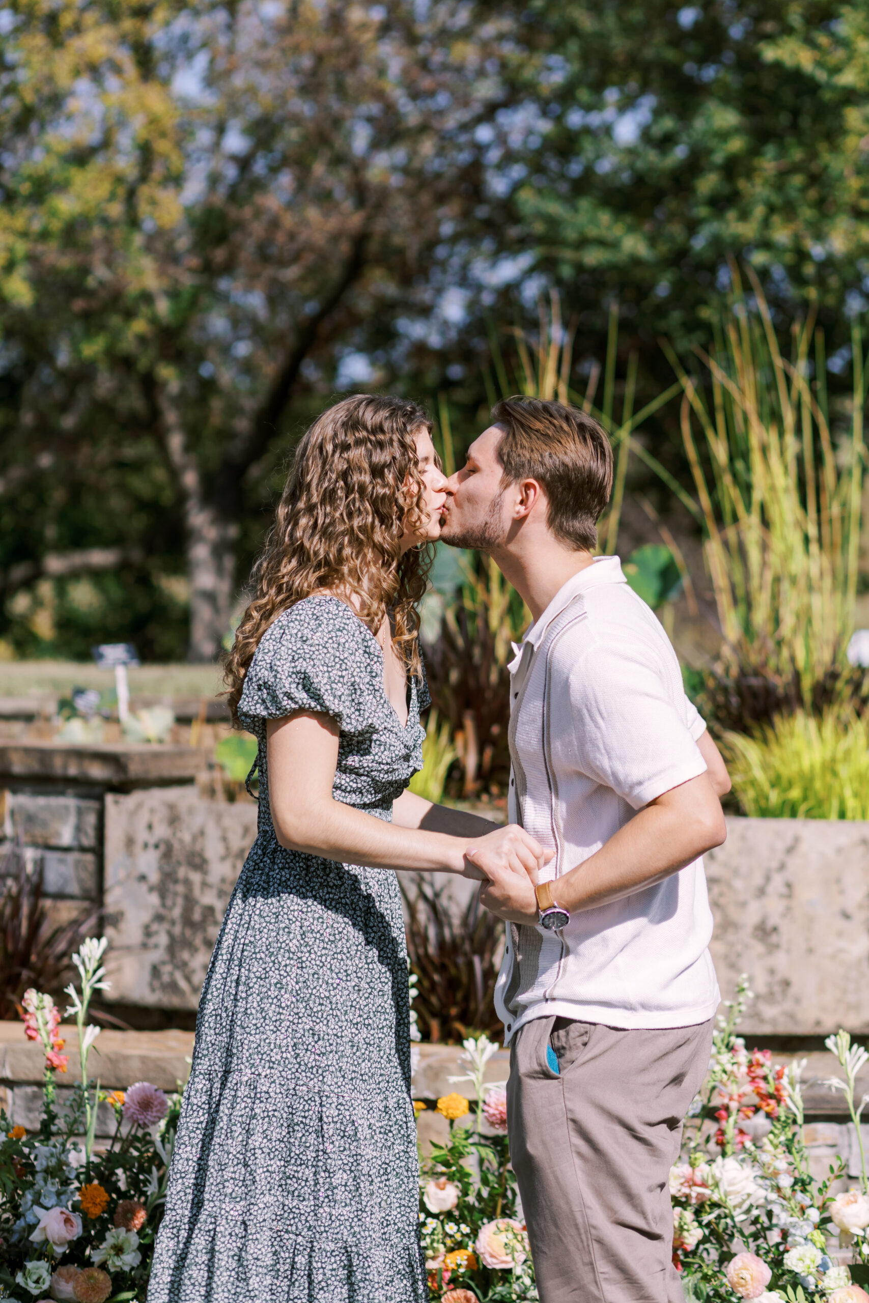 Couple share a kiss surrounded by flowers after engagement at Powell Gardens.