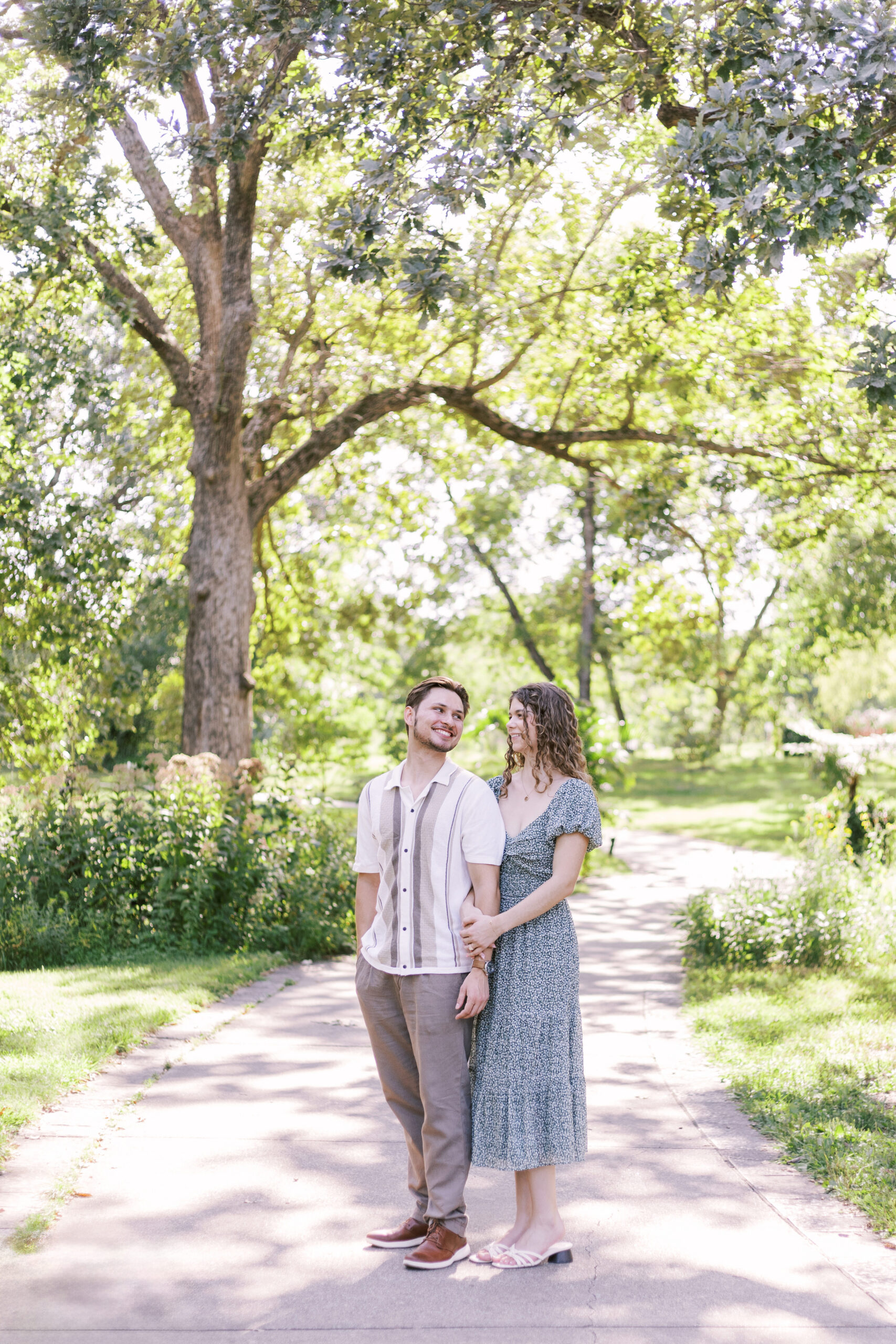 Couple walking hand in hand along tree-lined path at Powell Gardens after proposal.