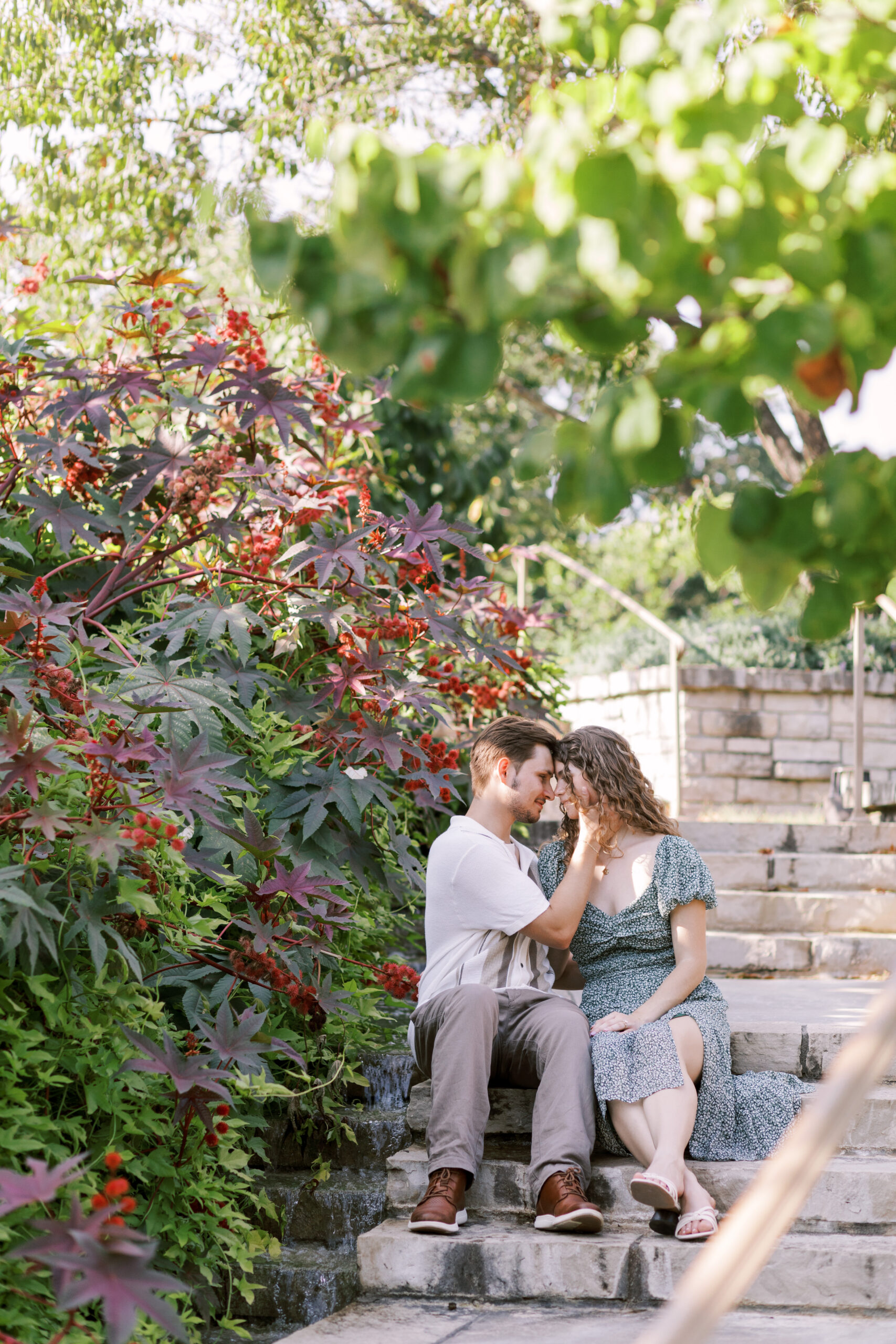 Couple sitting on stone steps surrounded by lush greenery, sharing an intimate moment after proposal at Powell Gardens.