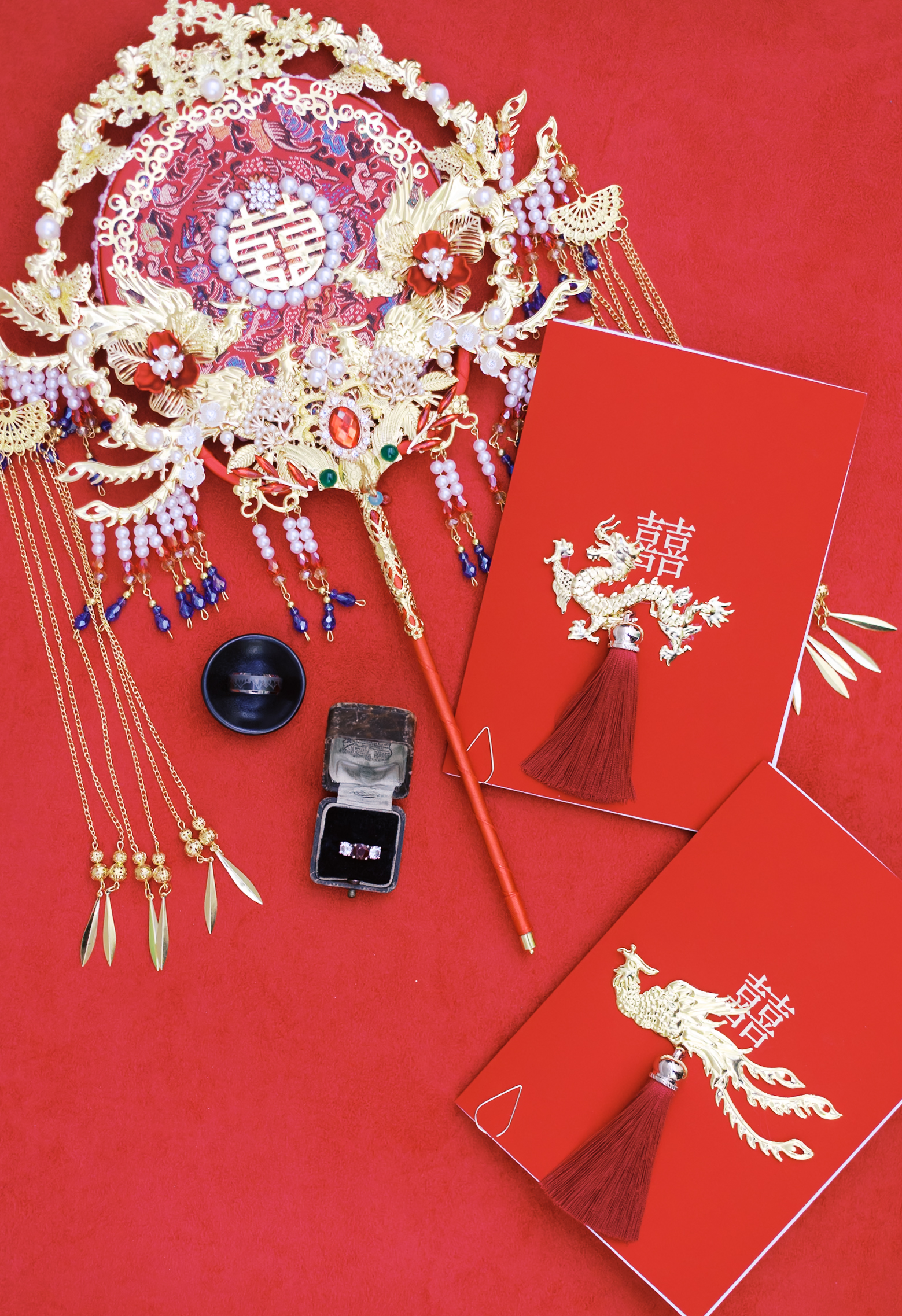 Traditional Chinese wedding accessories and red envelopes styled on a red backdrop with ornate gold bridal fan and jewelry.