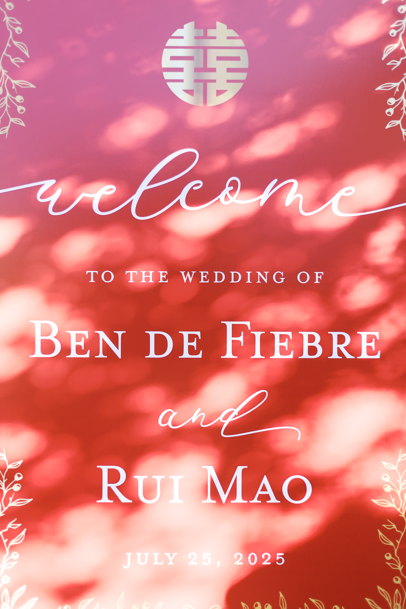 Red wedding welcome sign with white lettering for Ben De Fiebre and Rui Mao surrounded by soft sunlight patterns.