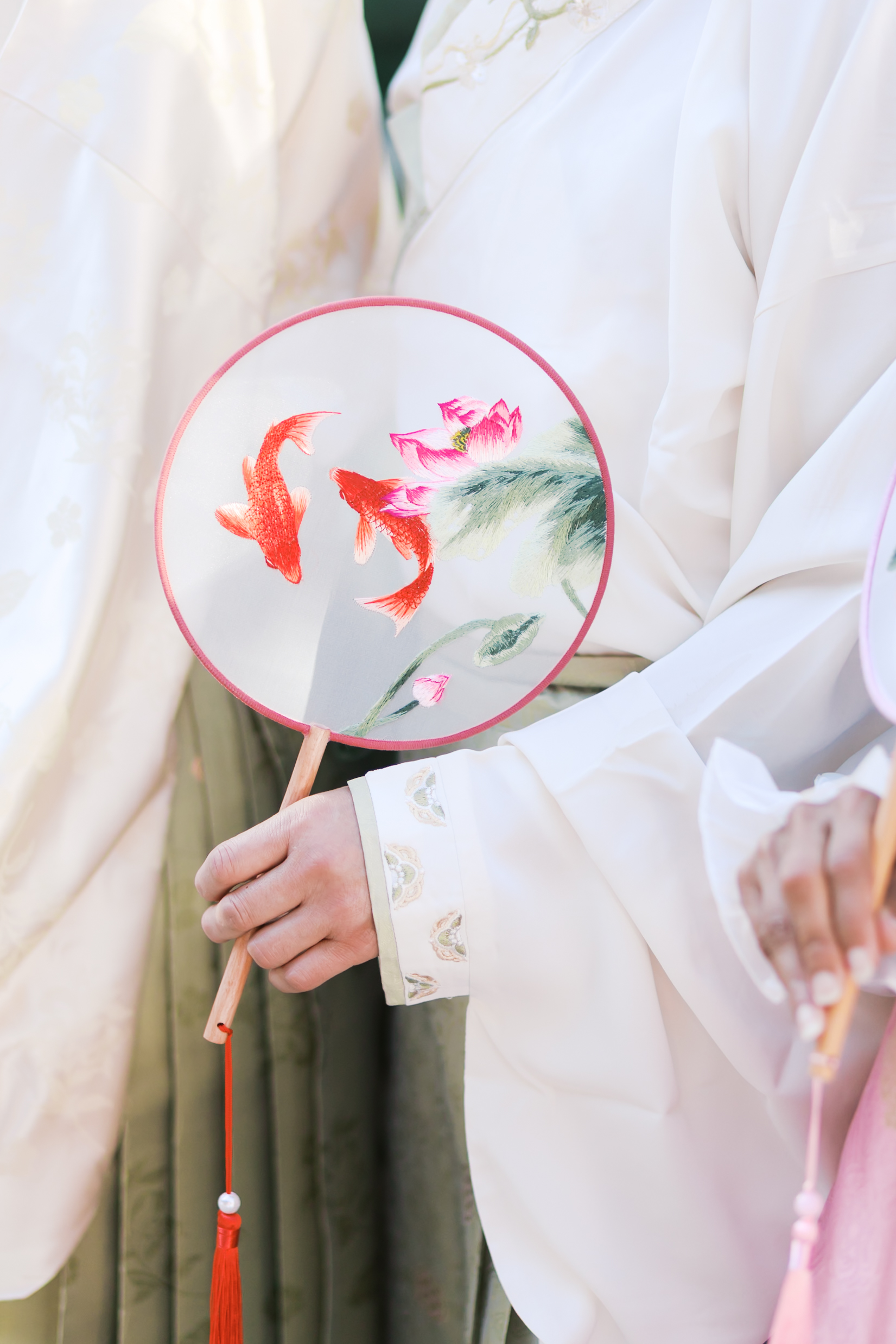 Hand holding a round silk fan painted with koi fish and lotus flowers while wearing traditional hanfu wedding attire.