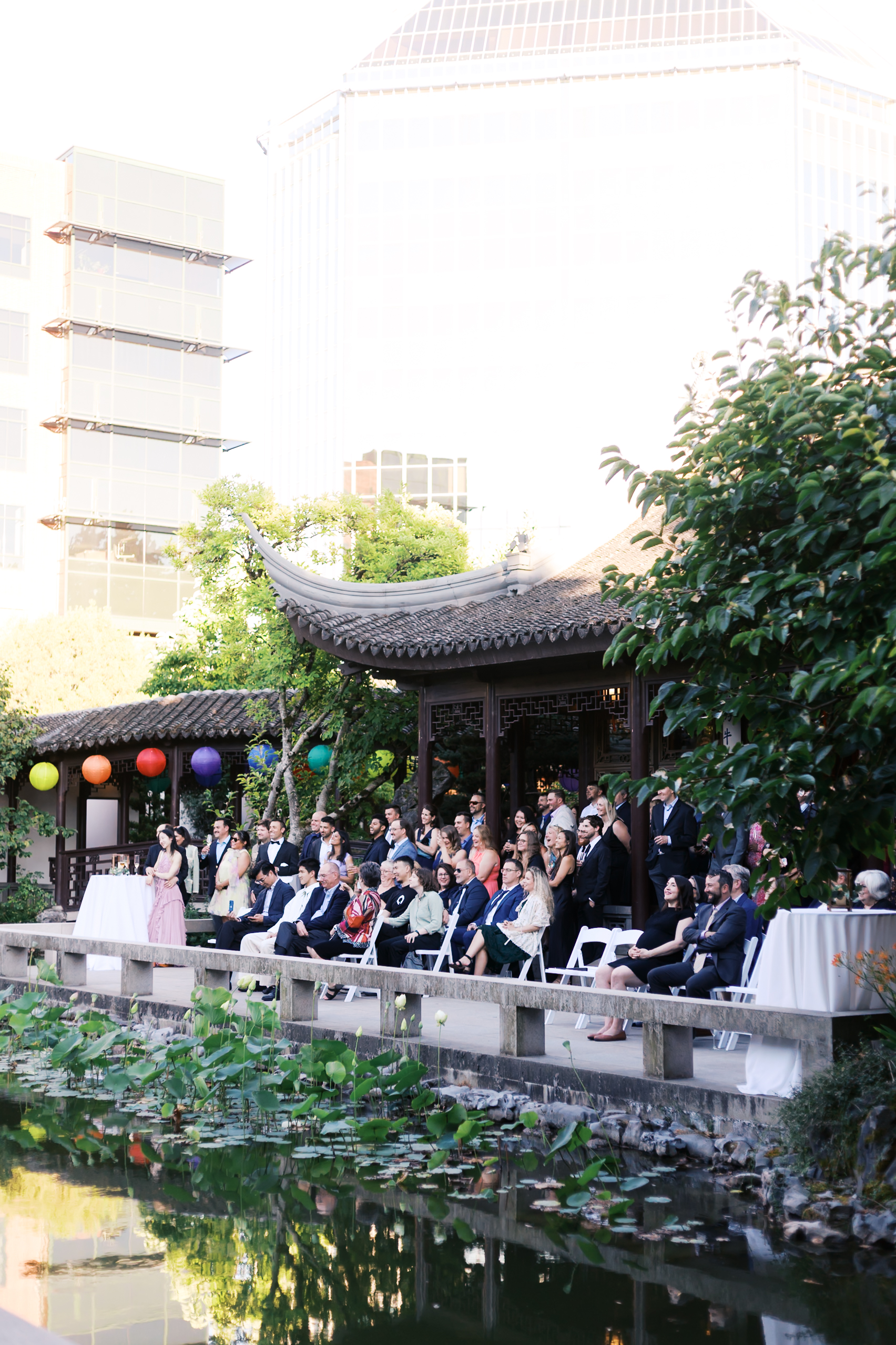 Wedding guests seated beside a pond during an outdoor ceremony at a traditional Chinese garden venue.