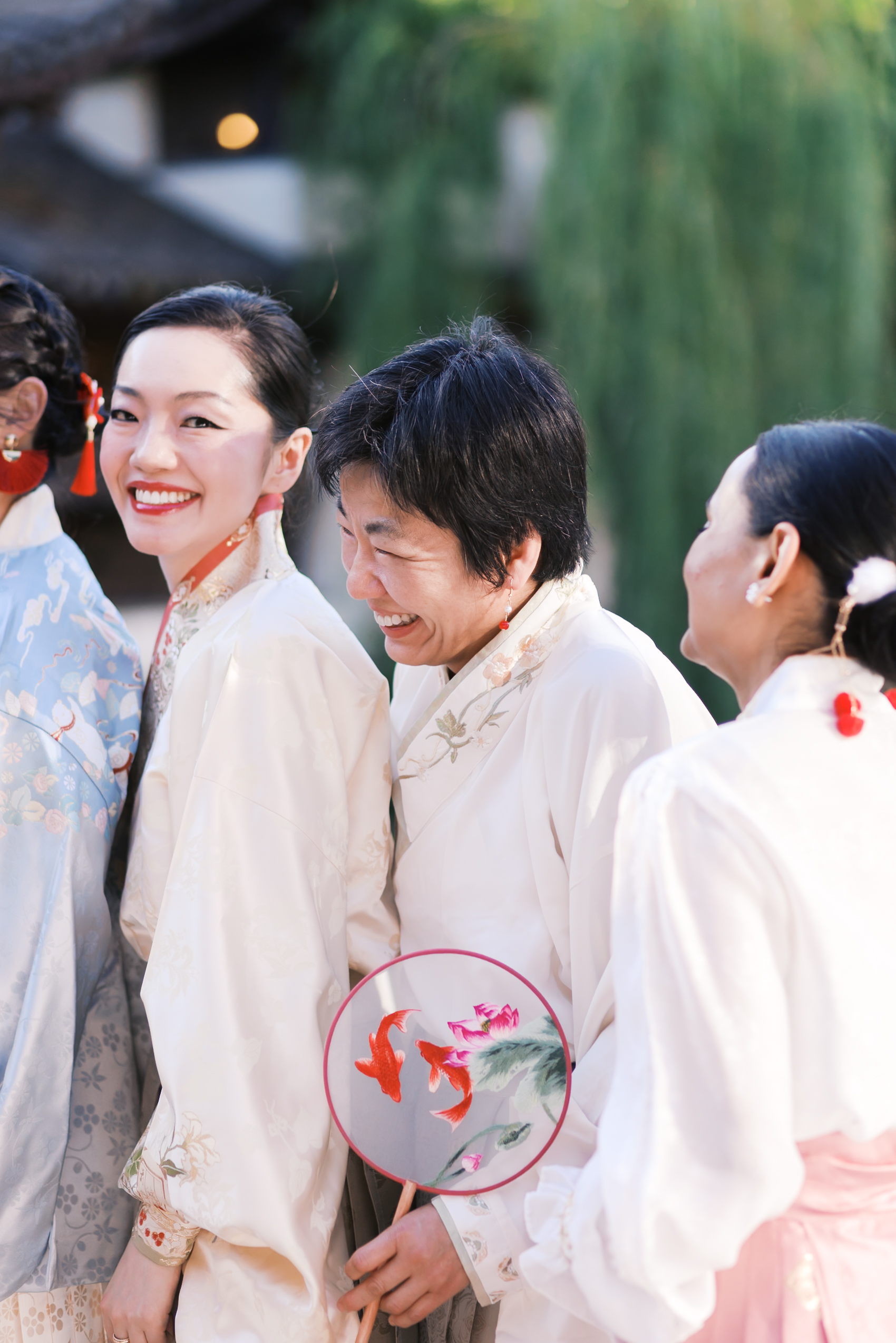 Wedding guests in embroidered hanfu smiling and chatting during outdoor garden celebration.