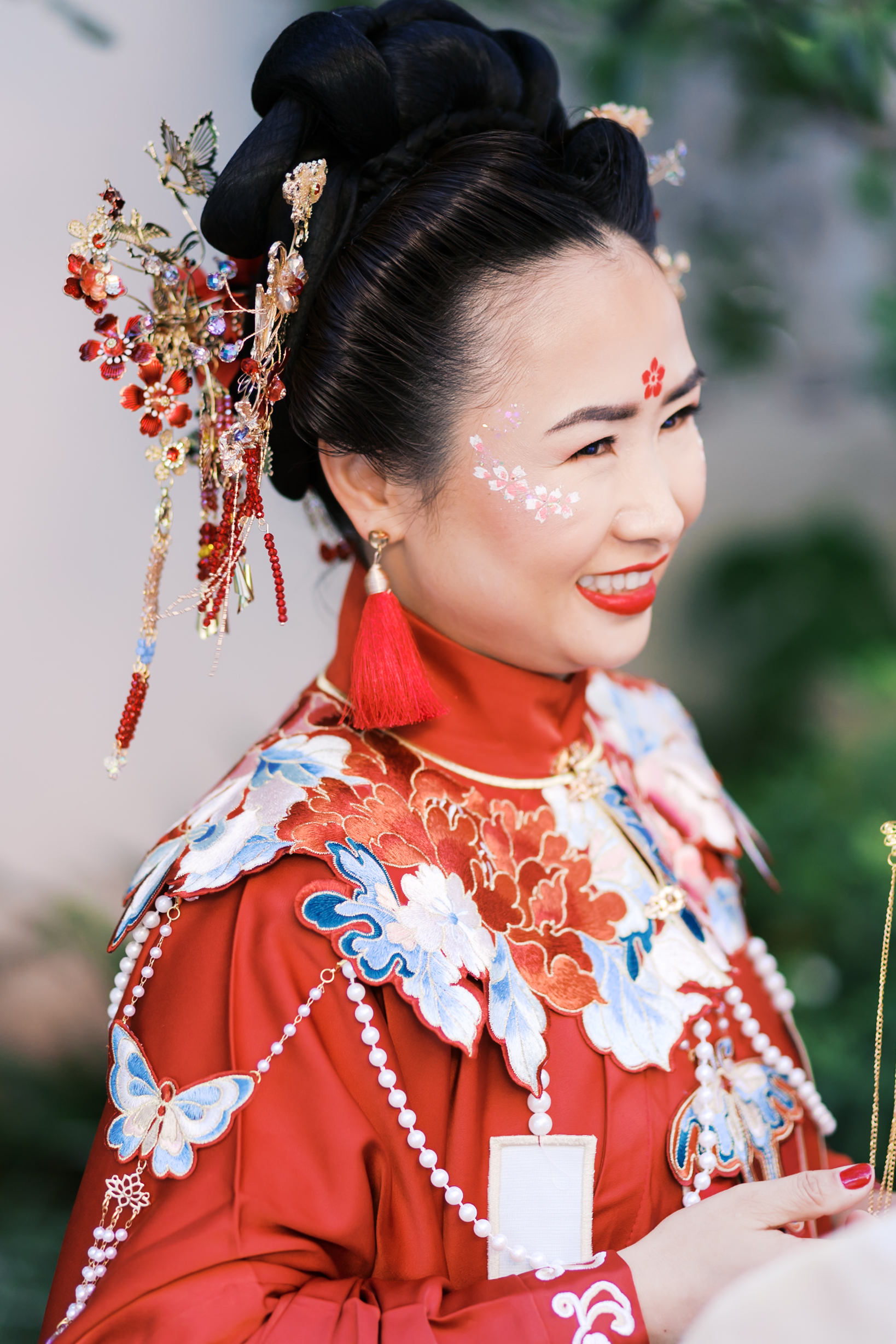 Bride in ornate red Chinese wedding attire with embroidered floral patterns and traditional hair accessories.