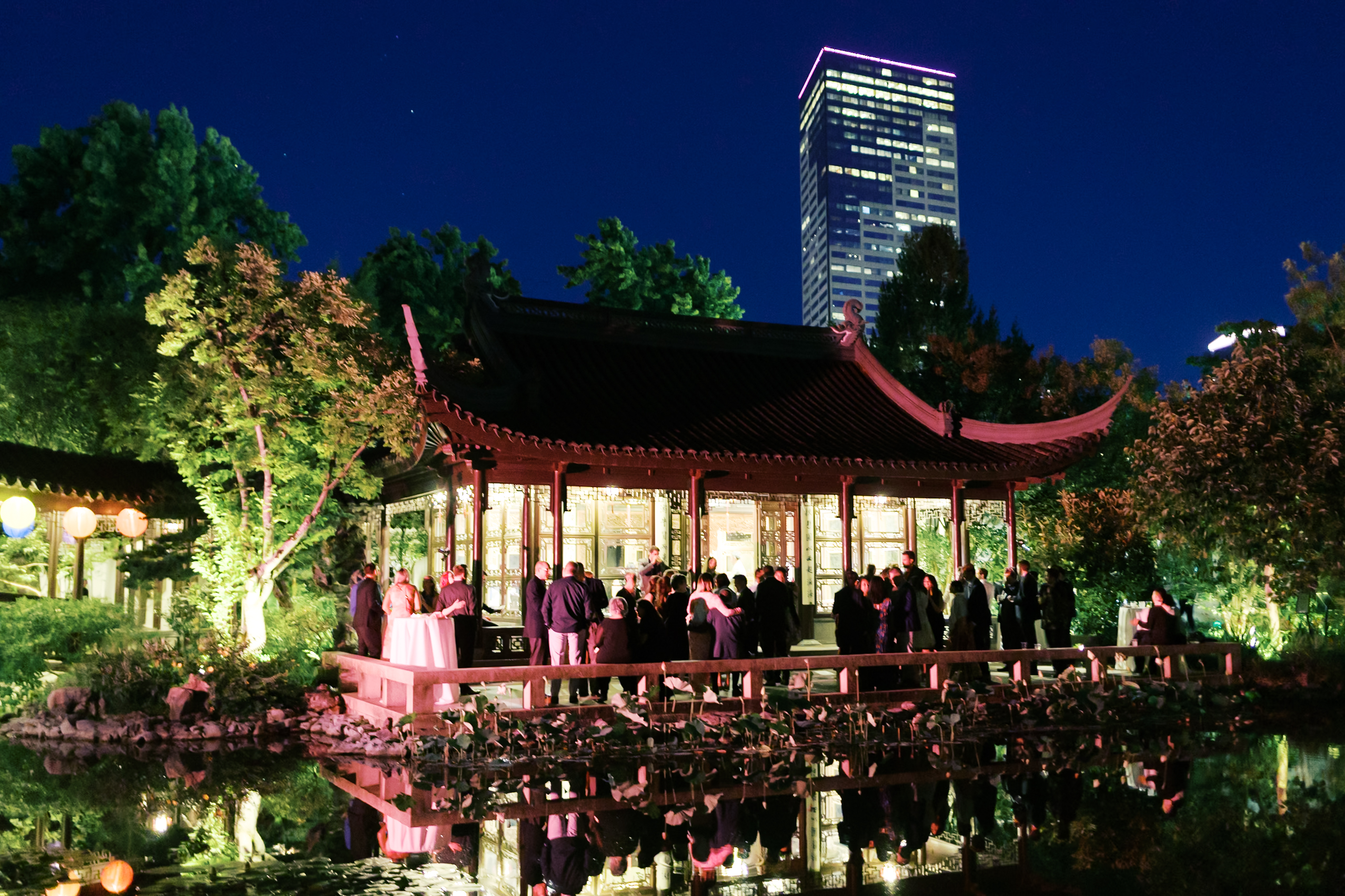 Nighttime wedding reception at a traditional Chinese pavilion reflected in a garden pond.
