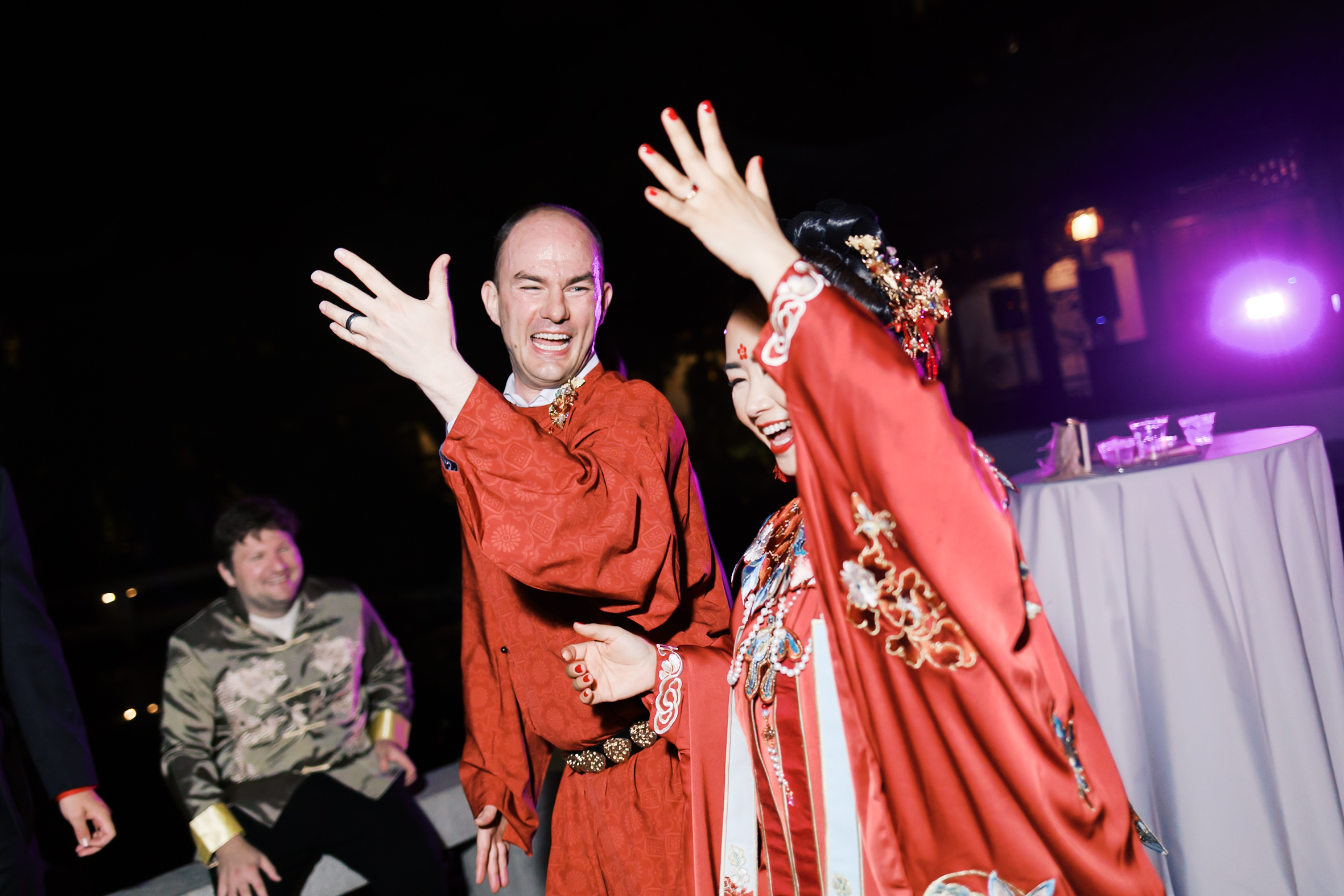 Bride and groom dancing together in matching red traditional Chinese wedding attire at night reception.