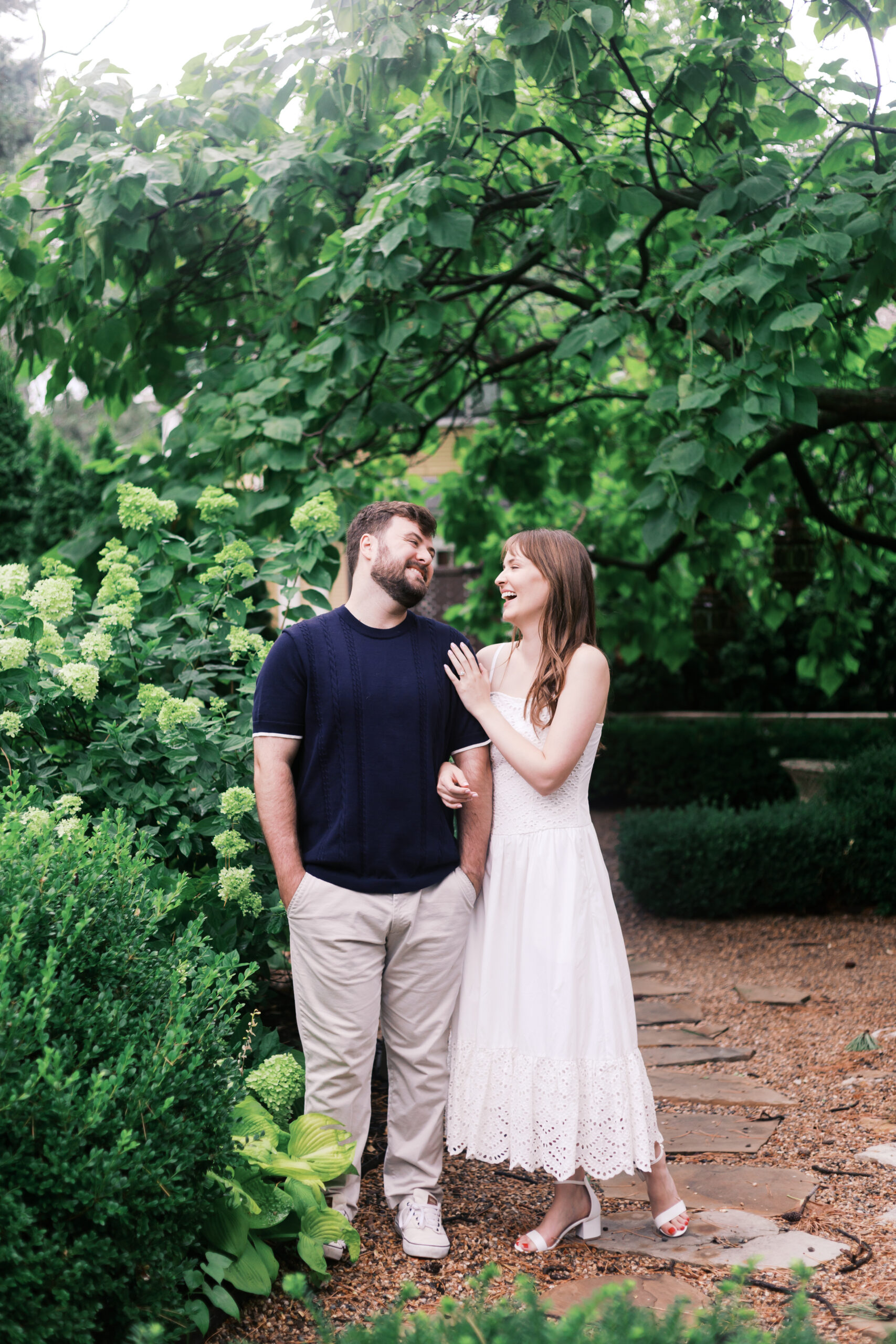 Engaged couple walking through a lush garden path during a romantic summer session.
