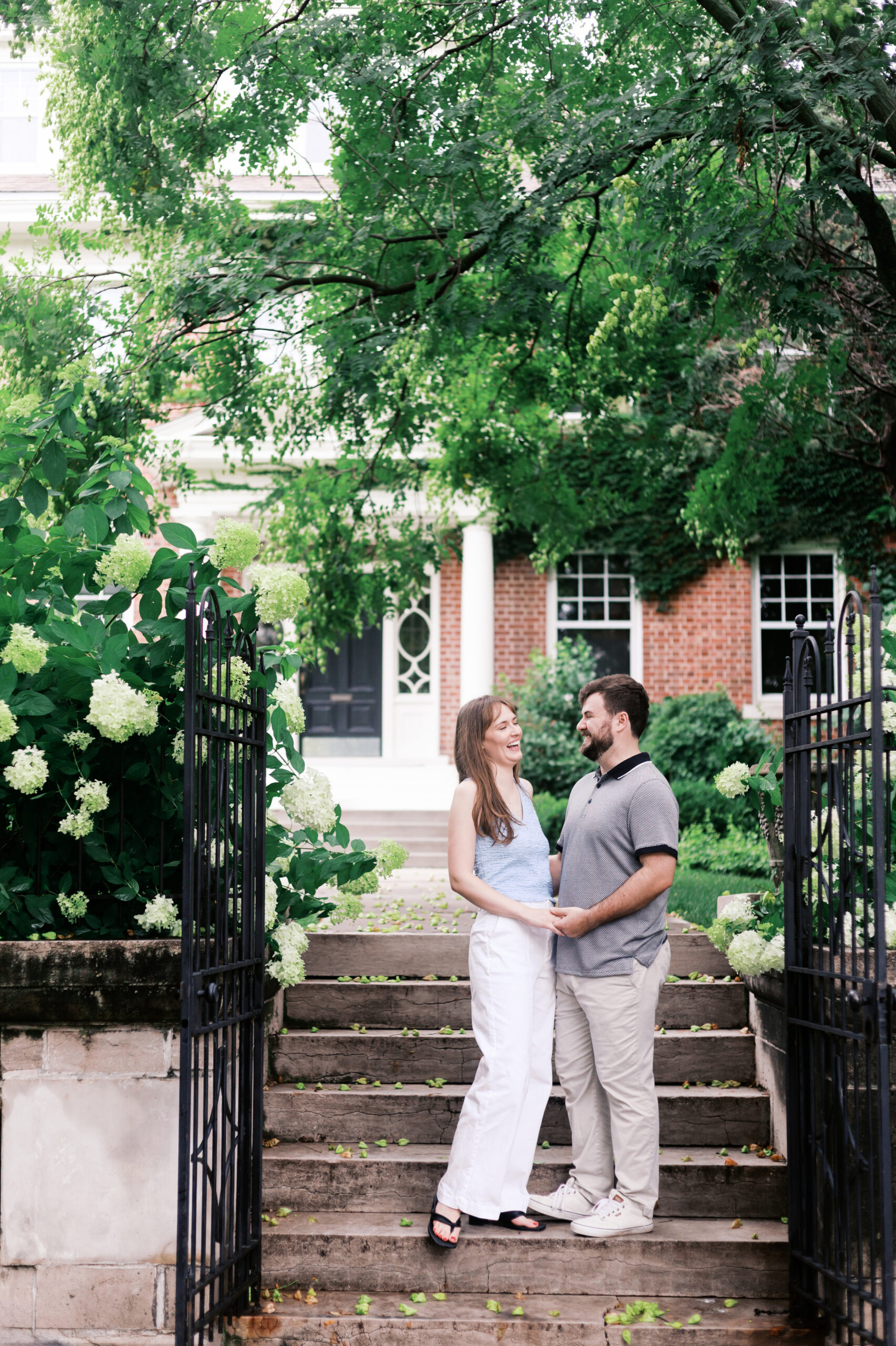 Couple laughing together on garden steps surrounded by blooming hydrangeas.