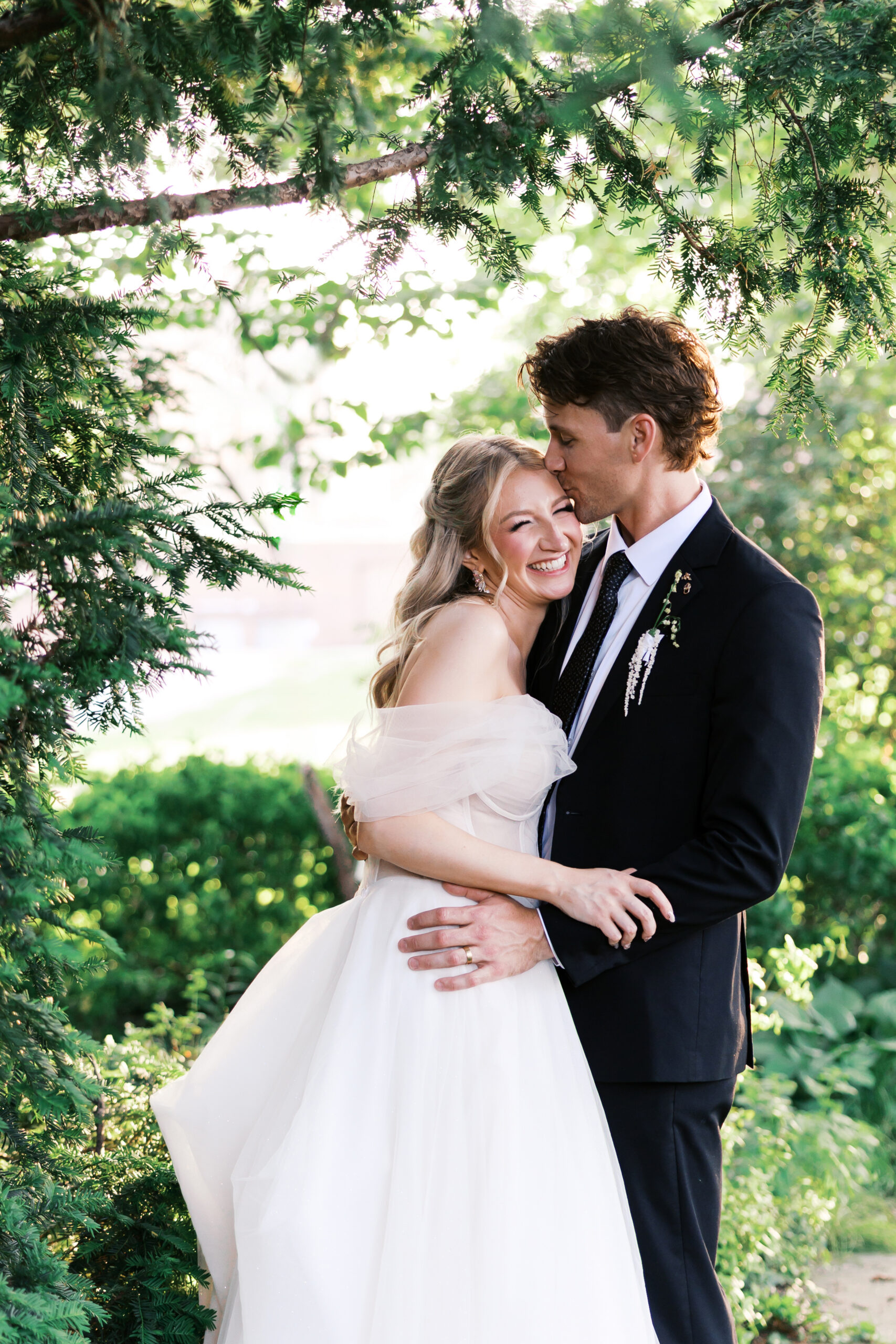 Bride laughing as groom kisses her forehead during romantic garden portraits at Simpson House.
