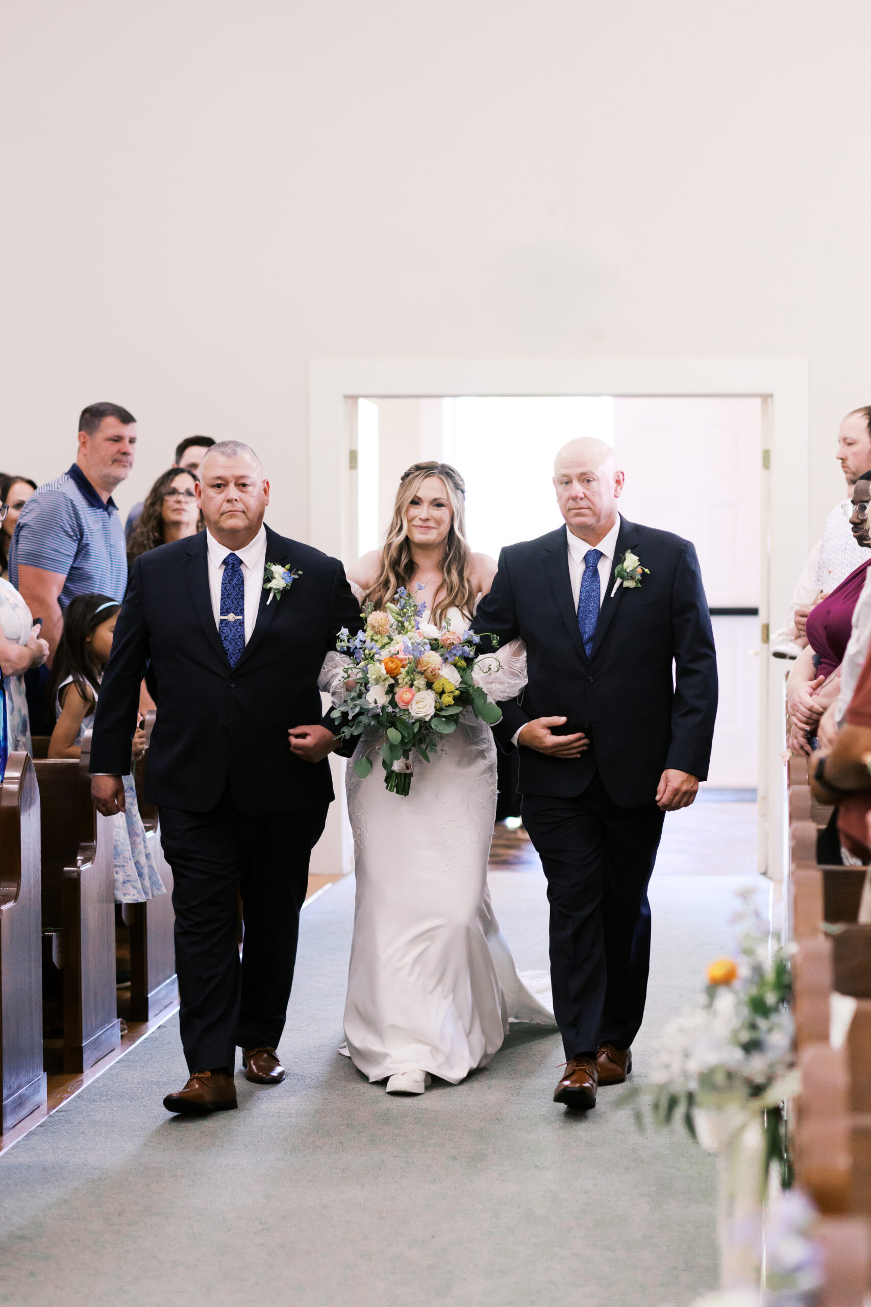 Bride walking down the aisle with two escorts while guests look on inside a church.