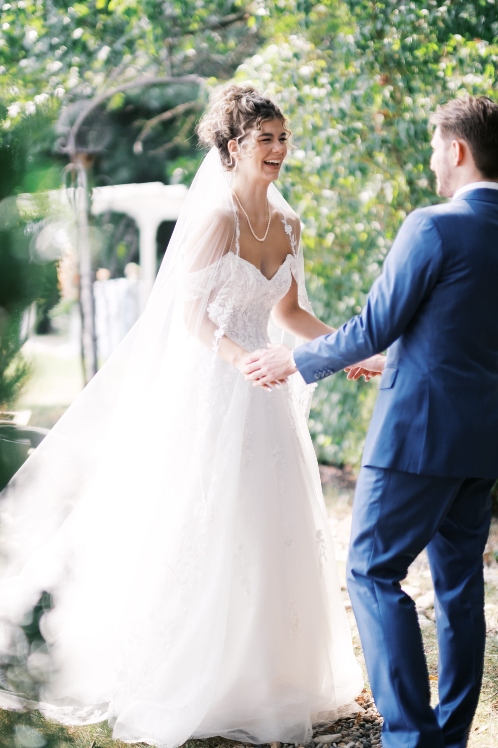 Bride and groom reaching for each other during an outdoor first look in a garden setting.