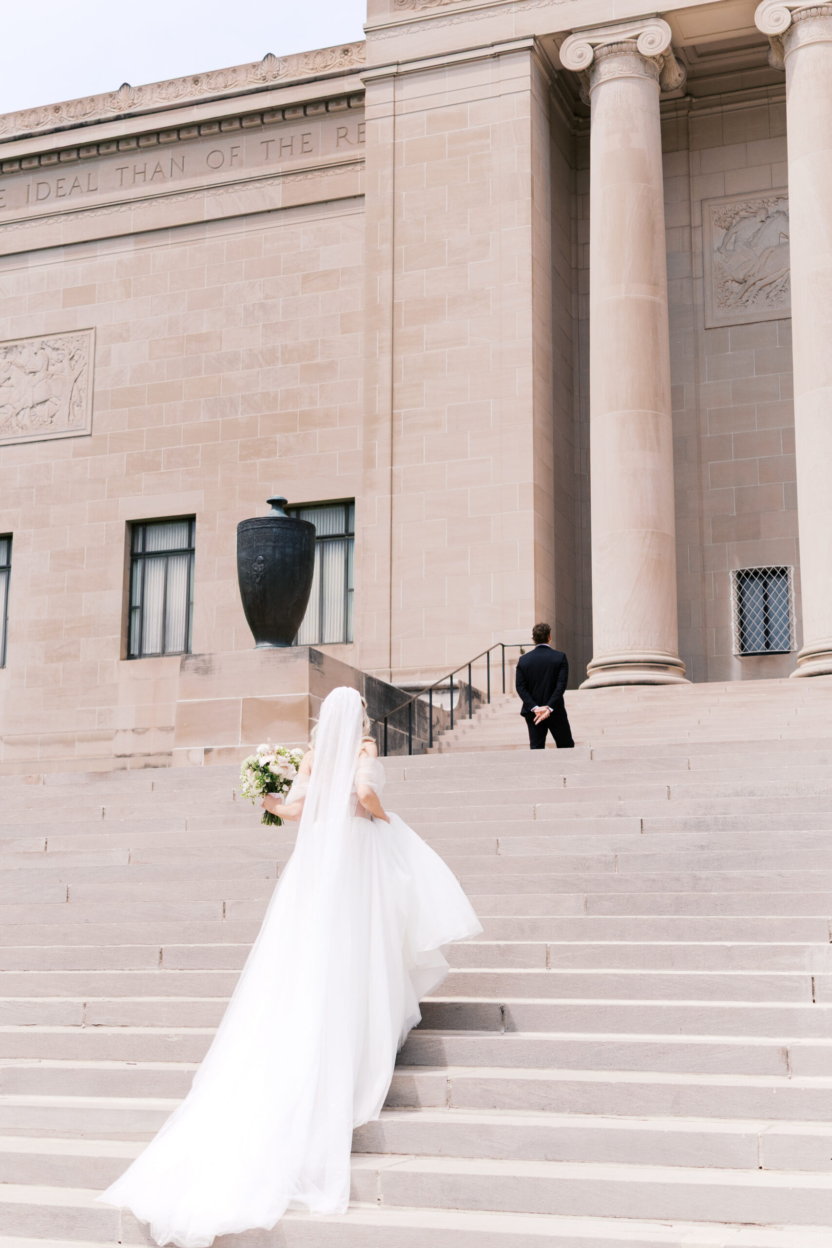 Bride walking up museum steps toward the groom for an outdoor first look.