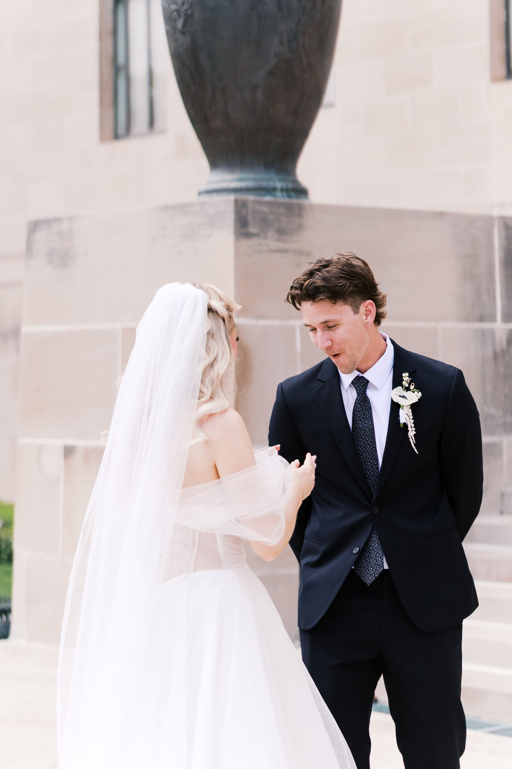 Groom reacting as the bride approaches him during an outdoor first look on museum steps.