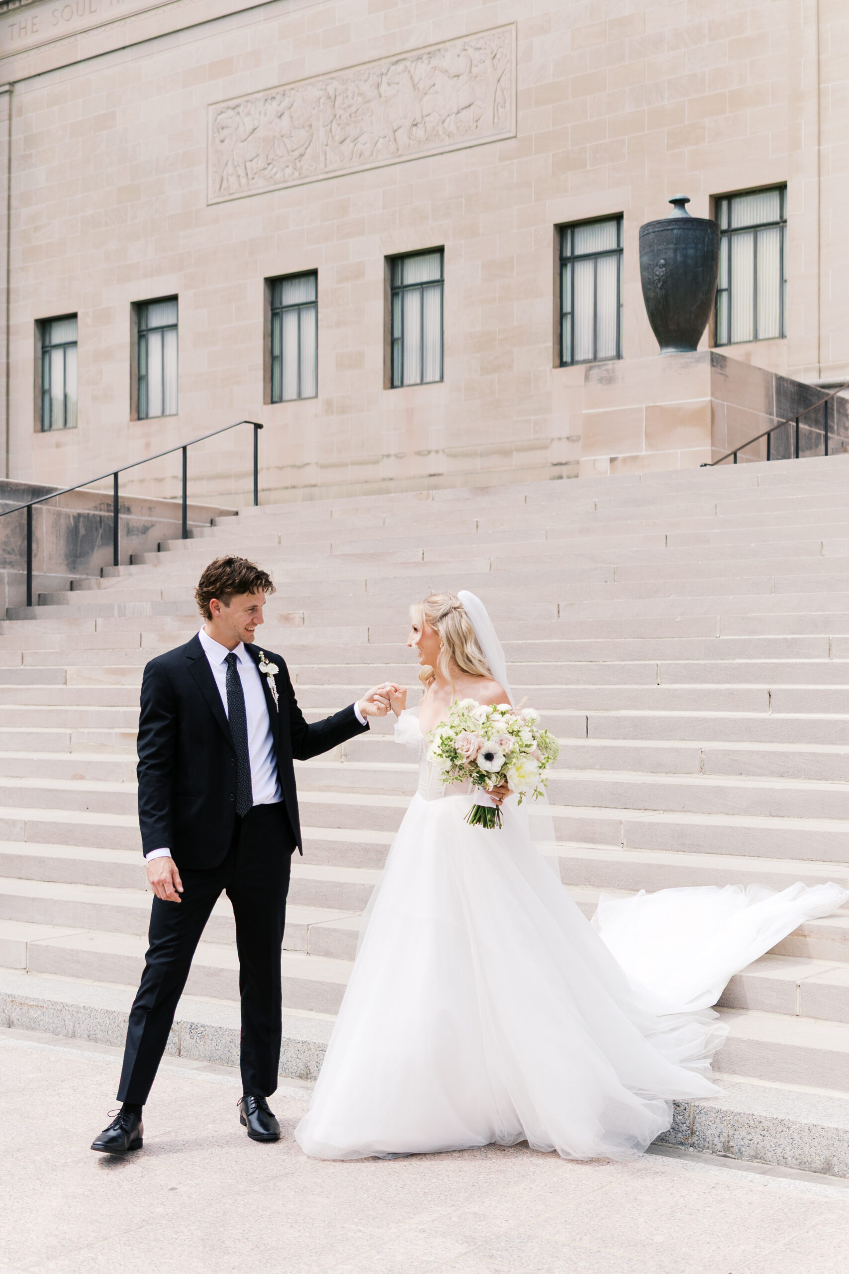 Bride and groom holding hands on wide stone steps outside a museum wedding venue.