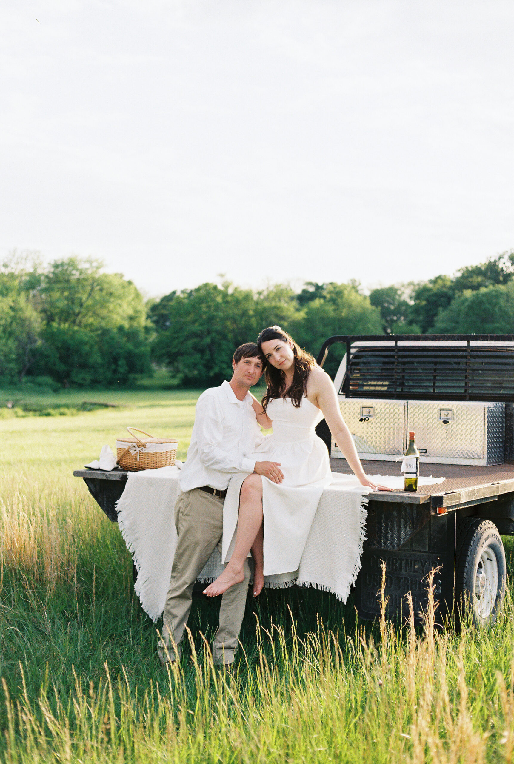Couple poses on a pickup truck for a countryside engagement session in a grassy field.