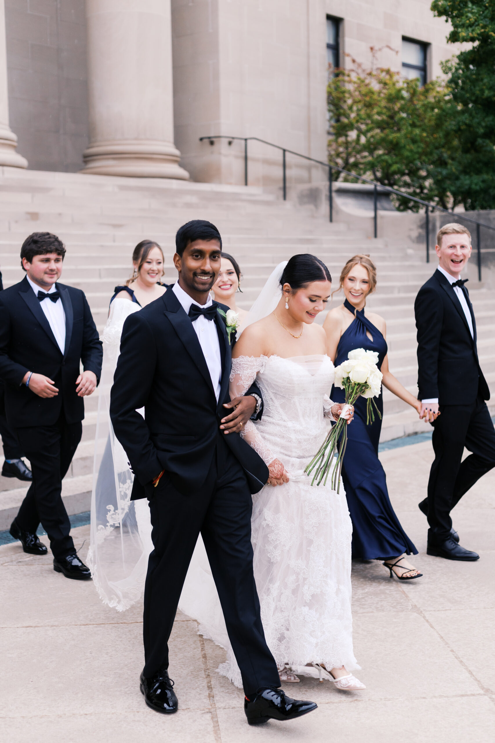 Bride and wedding party walk outside a classic building with stone steps.