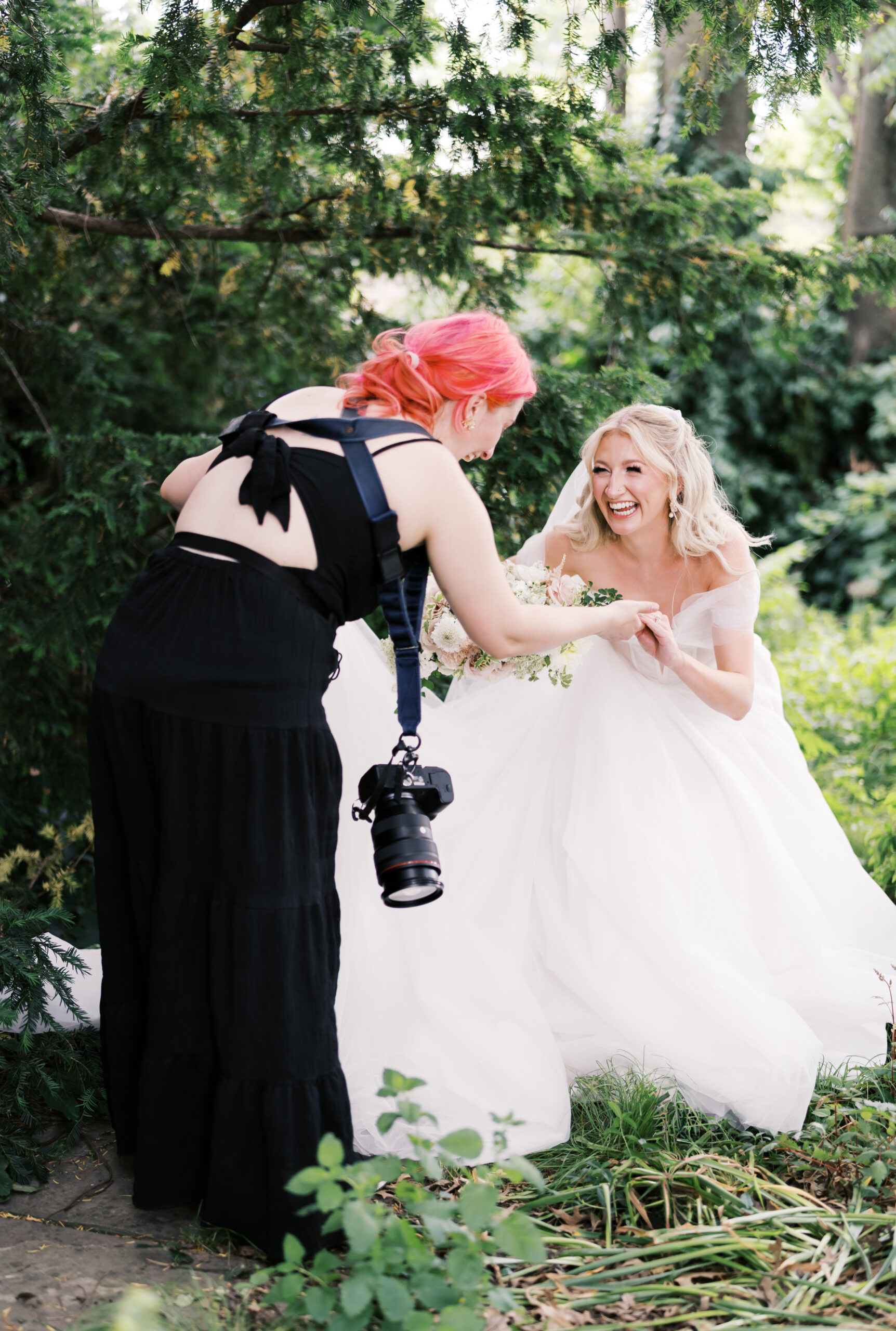 Photographer helps a bride adjust her dress during an outdoor bridal portrait session.