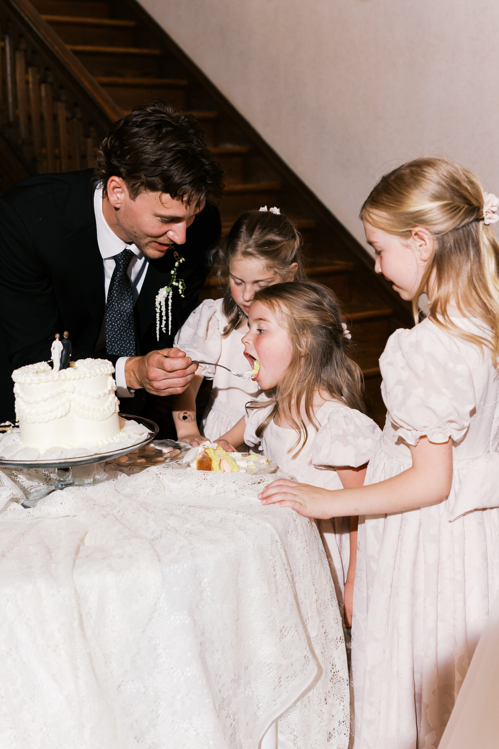 Groom feeds wedding cake to young children beside a small white cake.