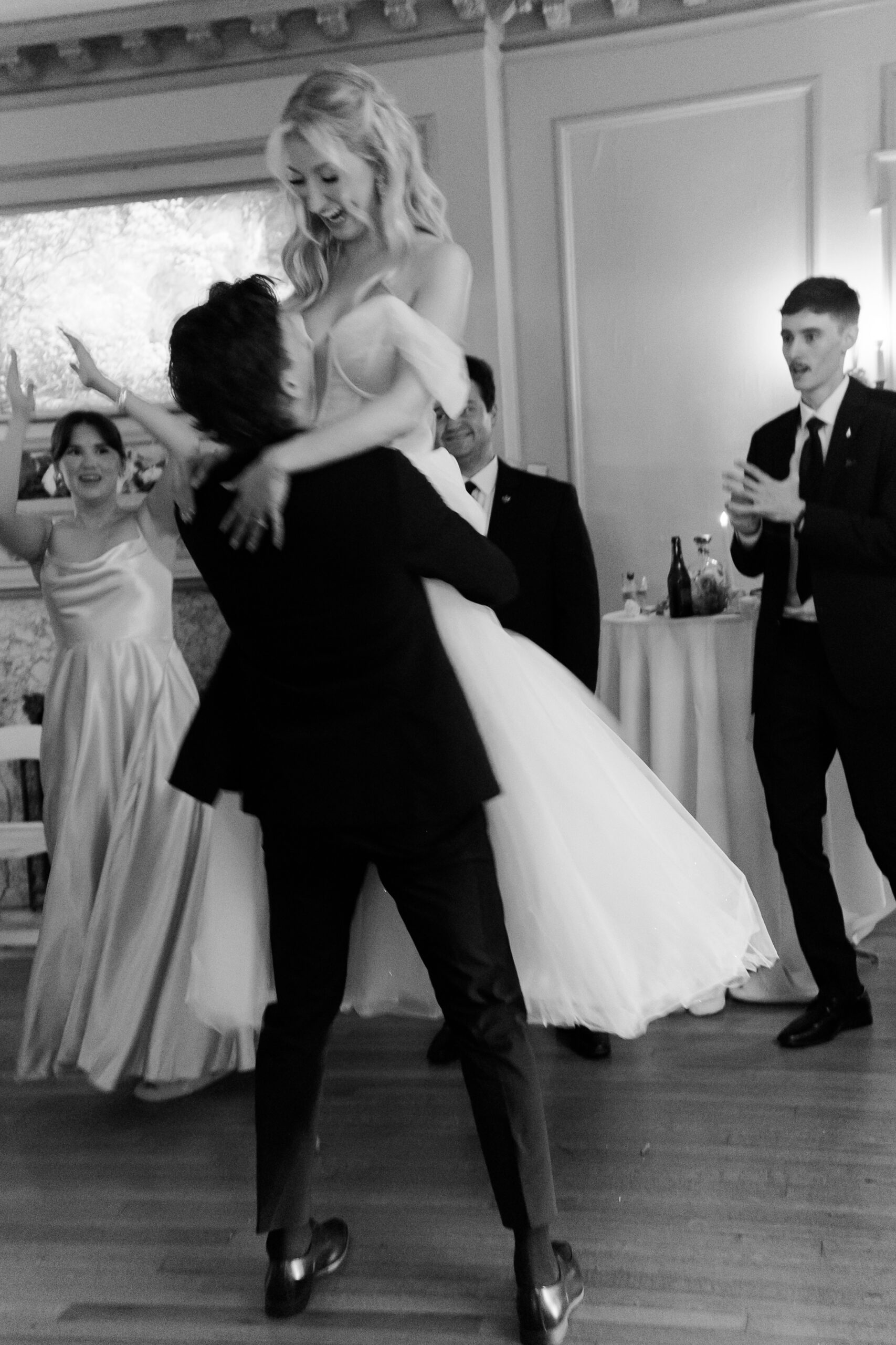 Black and white reception photo of a groom lifting a bride on the dance floor.