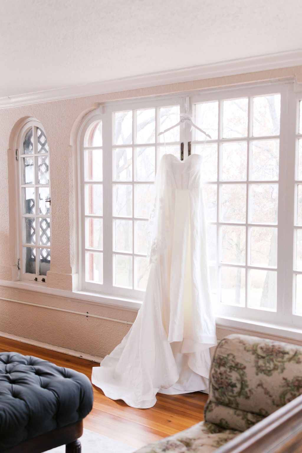 Strapless wedding dress hanging in front of large sunlit windows in Longview Mansion before the bride gets ready.